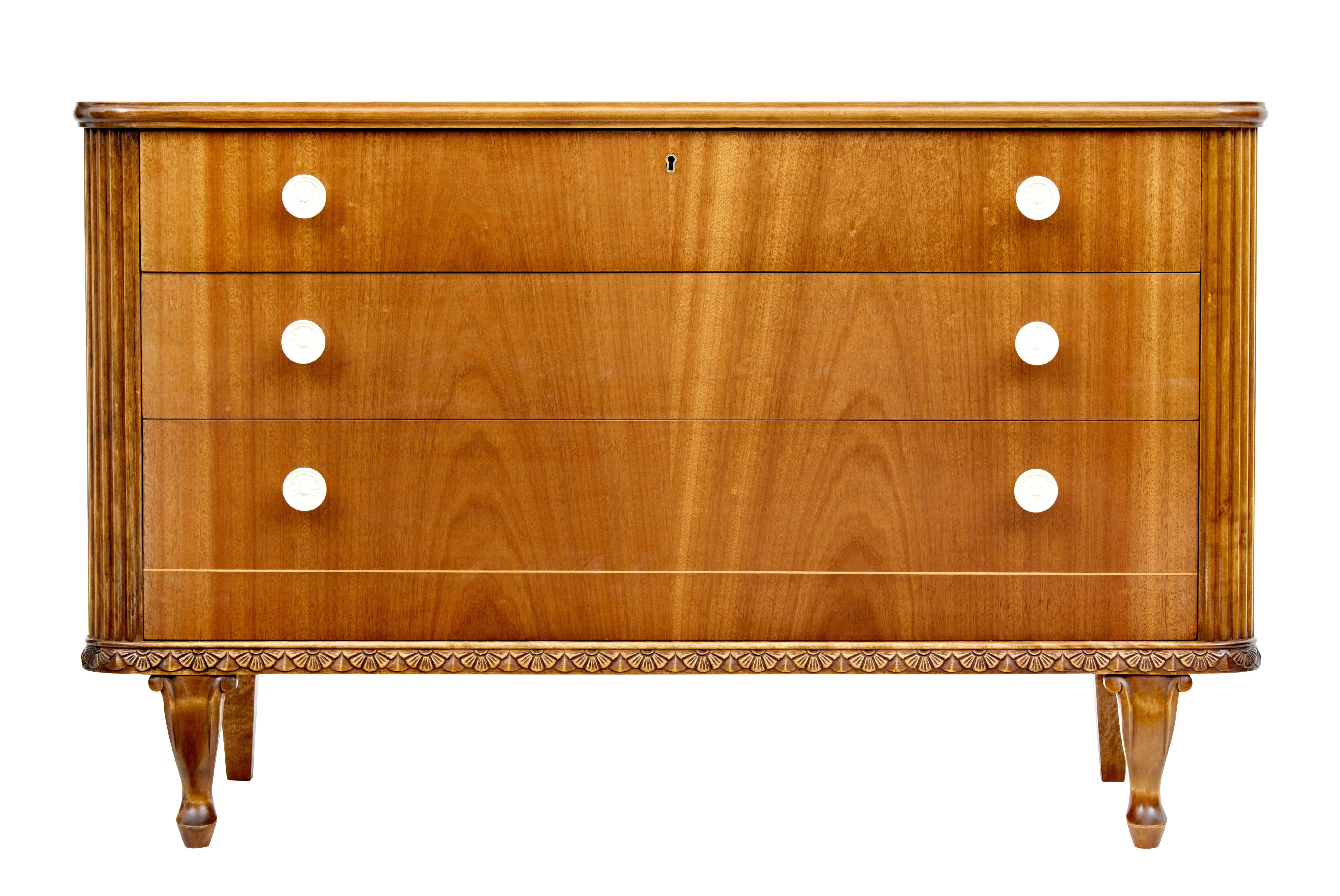 Elegant 1950s Scandinavian modern teak chest of drawers.

Graduating three drawers which are flanked either side by fluted sides. Bottom door with contrasting stringing detail. Carved apron below the drawers. Standing on scrolling front legs and