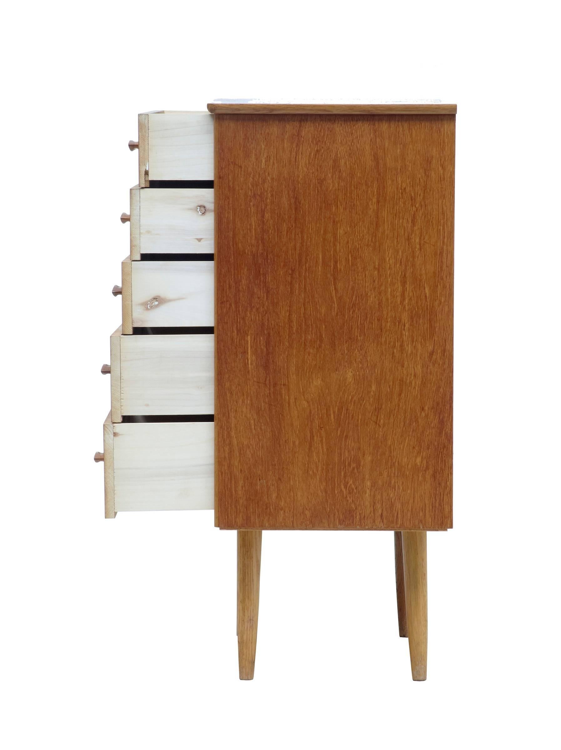 Small five-drawer chest of drawers, circa 1960. Fitted with contrasting light oak handles. Light veneer damage to four-drawer (photographed) surface marks and staining to top surface.

Measures: Height: 28 1/2