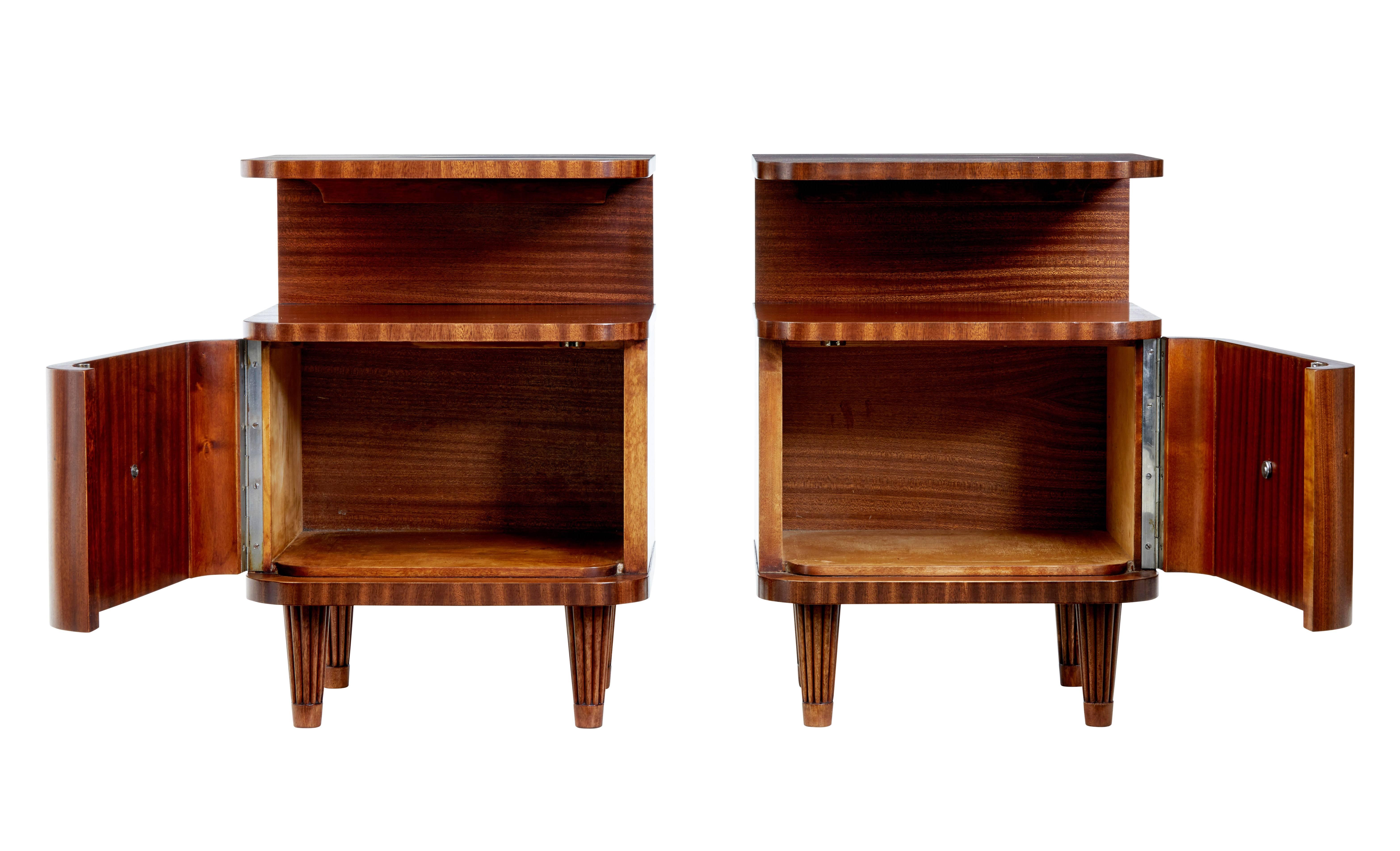 Good quality pair of Swedish Scandinavian modern bedside tables circa 1960.

Over sailing top surface with single door cupboard.  Brass handle to door front.

Standing on fluted tapering legs.