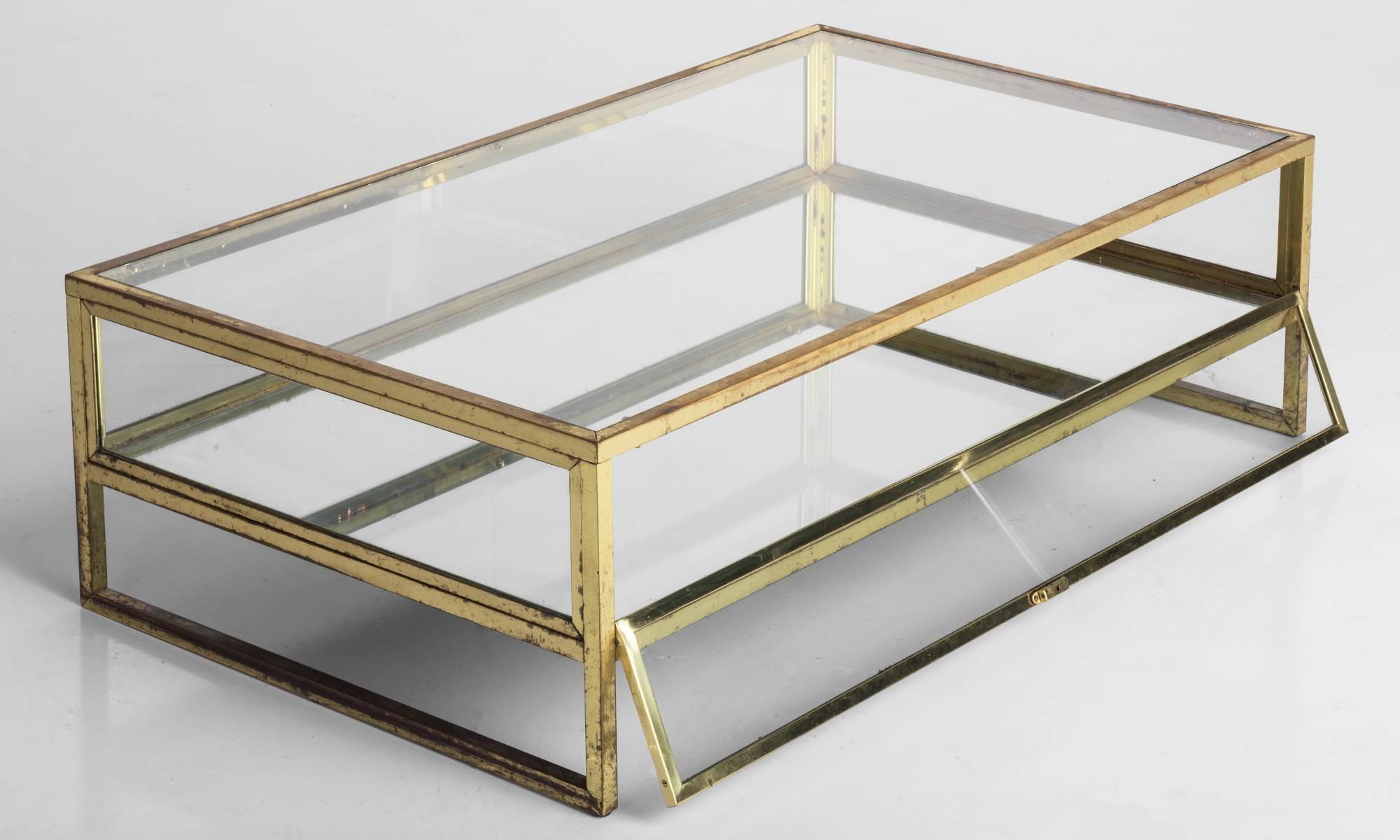 Brass and glass coffee table, circa 1970.

Elegant brass framework with internal compartment, featuring mirrored glass base.

Measures: 47" L x 27.5" D x 14" H.