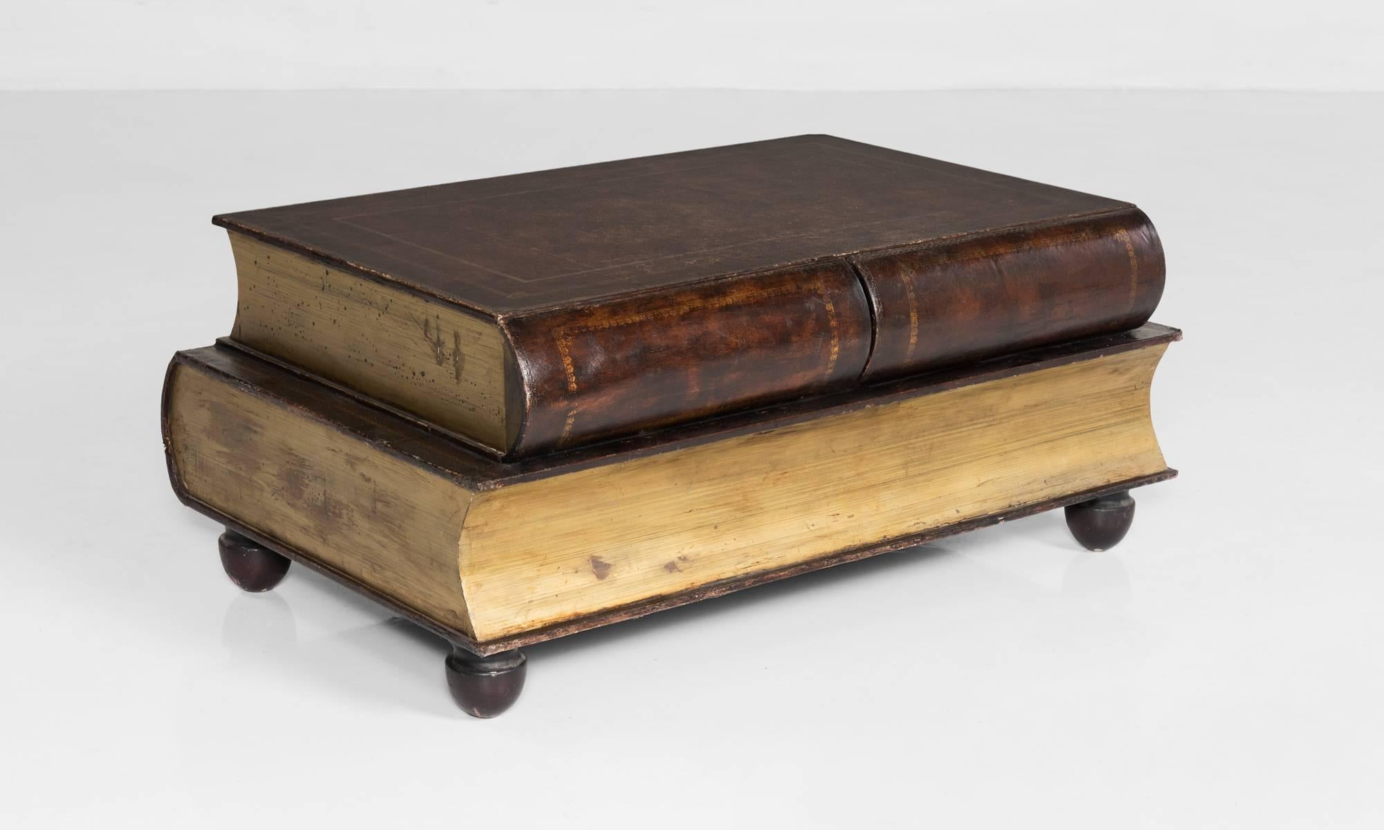 Leather cladded book coffee table, made in England, circa 1950.

Two trompe l’oeil painted staggered book forms feature two hidden drawers.