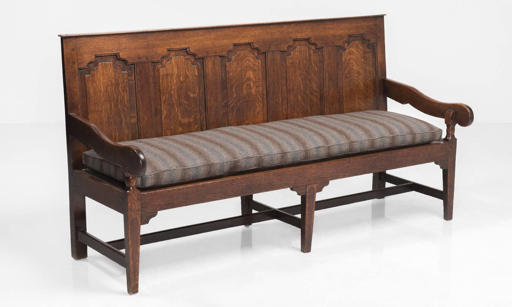 Georgian oak settle, Made in England, circa 1780.

Handsome oak bench with shaped and raised panels to the back. Each leg is inlaid with a mahogany panel on the front face. Long cushion upholstered in Maharam wool.