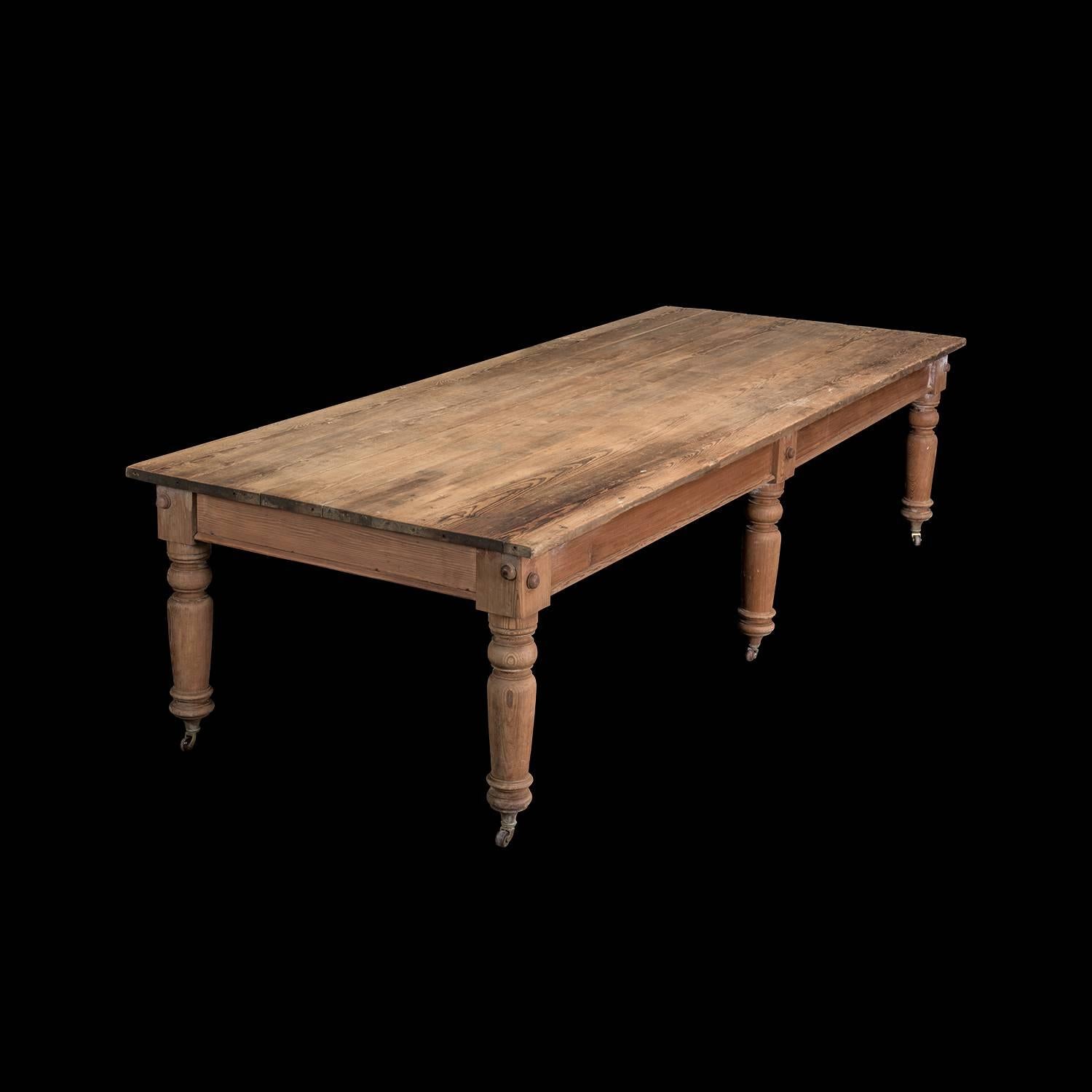 An extremely large mid-19th century scrubbed pine six-legged table, standing on castors (three original, three later) with plenty of leg room, worn and well weathered.