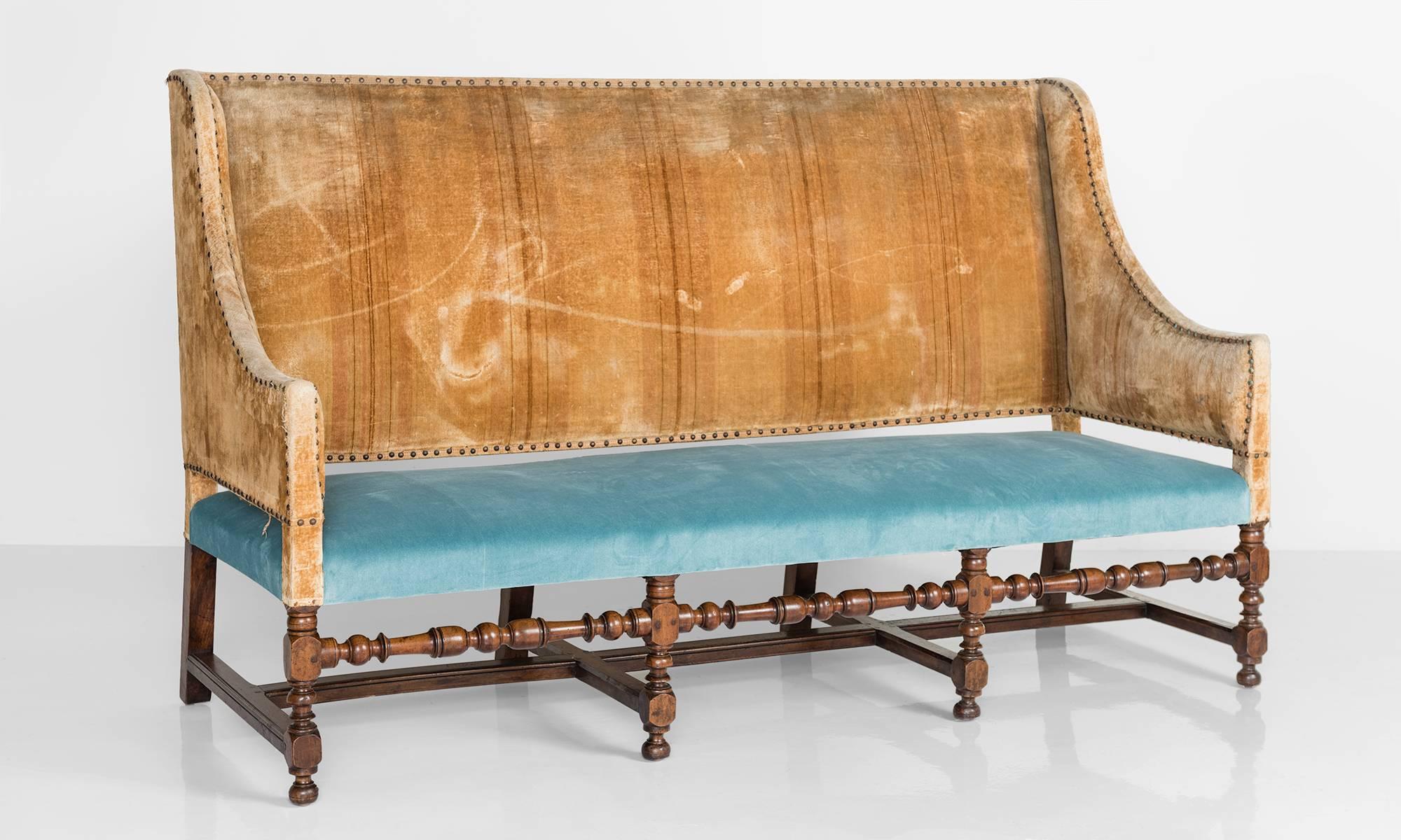 Early French sofa with carved wooden legs and velvet upholstery.