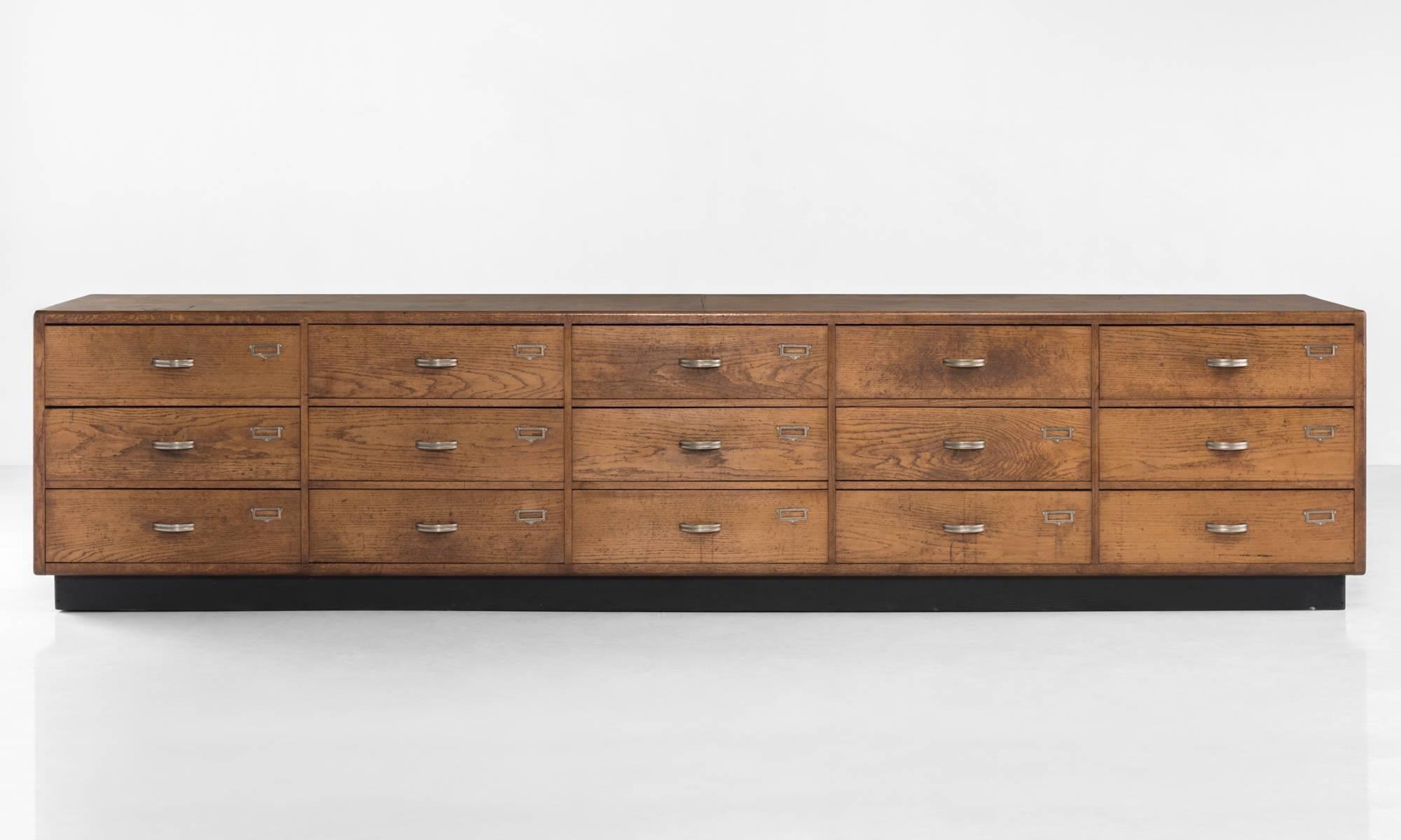 Massive oak chest of drawers
France, circa 1950.

15 drawers with original brass hardware on black base.