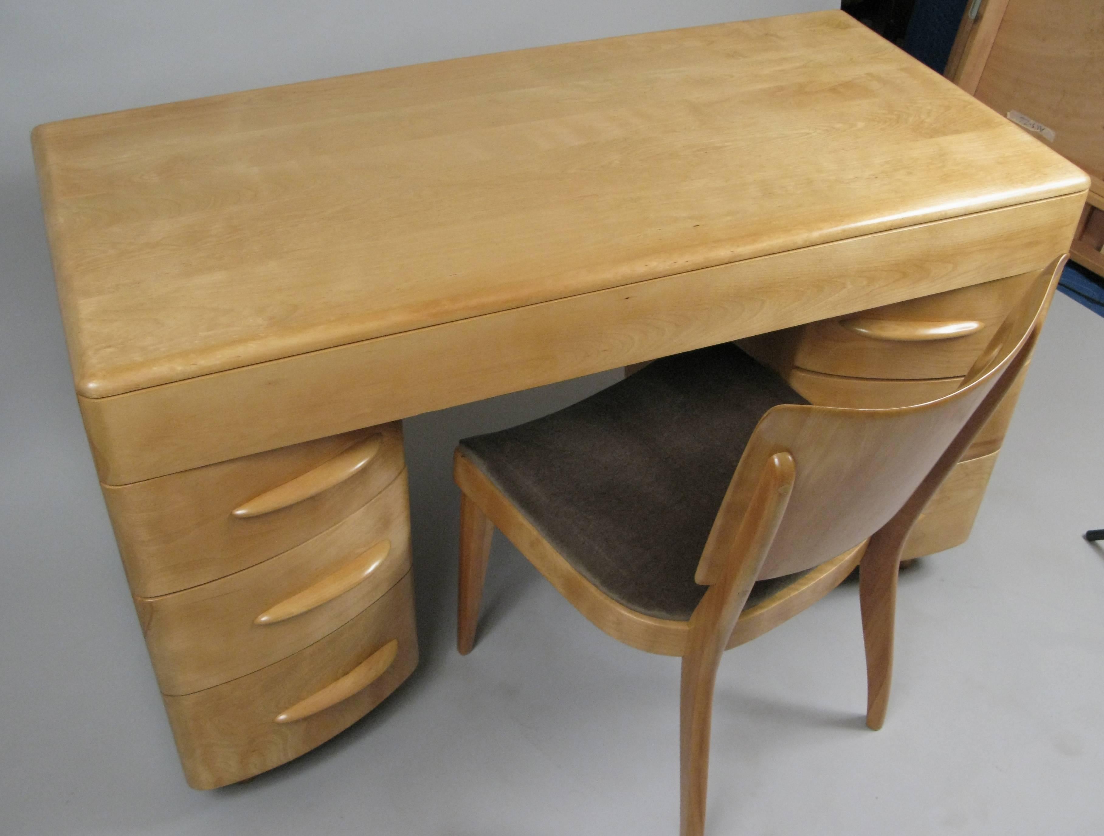 A Classic kneehole desk in solid birch made in the 1950s by Heywood Wakefield, along with a companion 'sharkfin' desk chair also by HW. The desk has a full width pencil drawer across the top and drawers on both sides. Both the desk and chair have