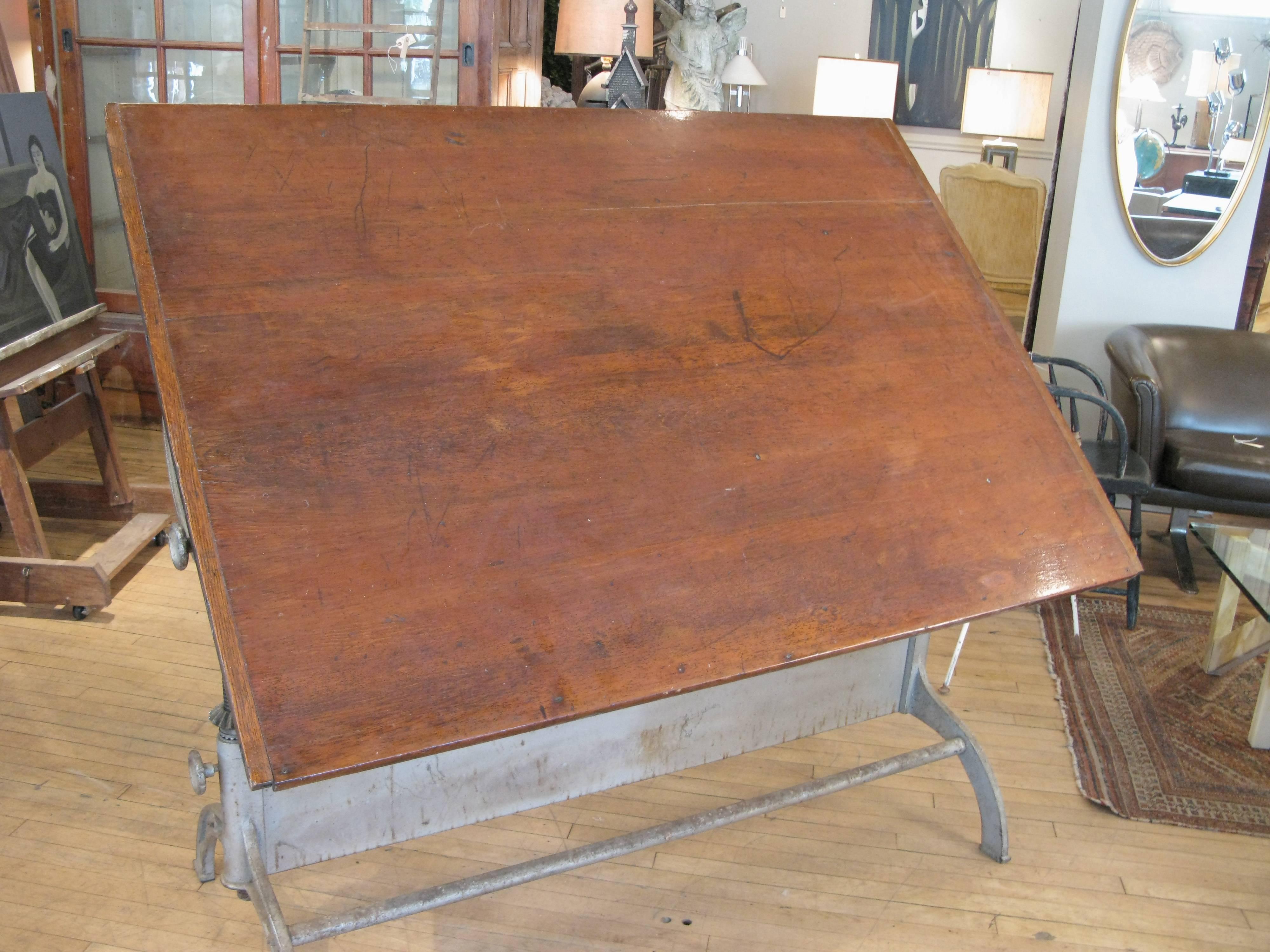 A very handsome antique 1920s fully adjustable drafting table with a cast iron base and large work surface. The top is tilt and height adjustable with a cast iron wheel in the center of the frame. Very well made and stabile, the top can be set as a