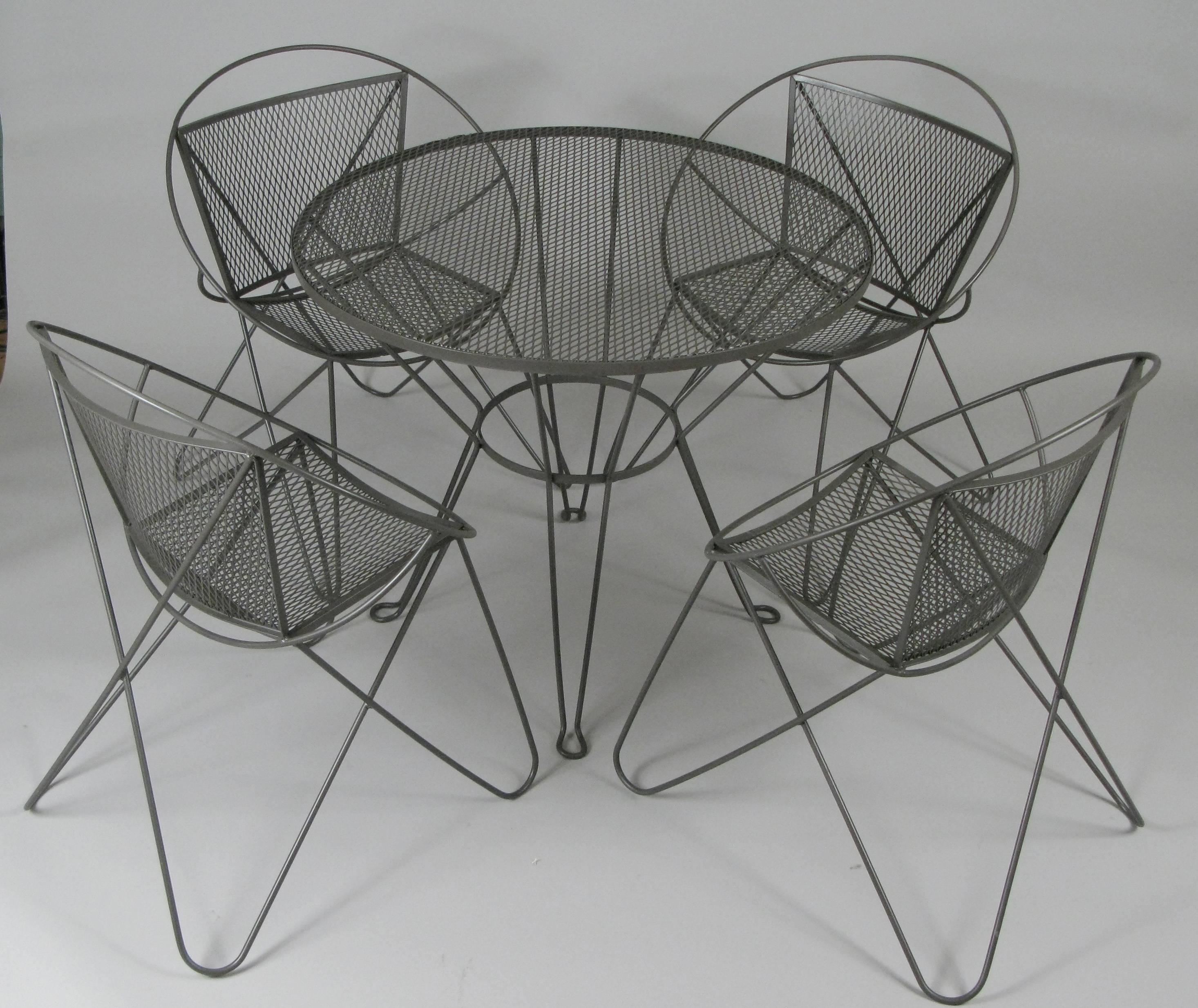 A very nice vintage 1960s wrought iron garden dining set by Woodard, with four chairs with iron hairpin frames and steel mesh seats and backs, and a round dining table, as well as a companion small round drinks table. The whole set has just been