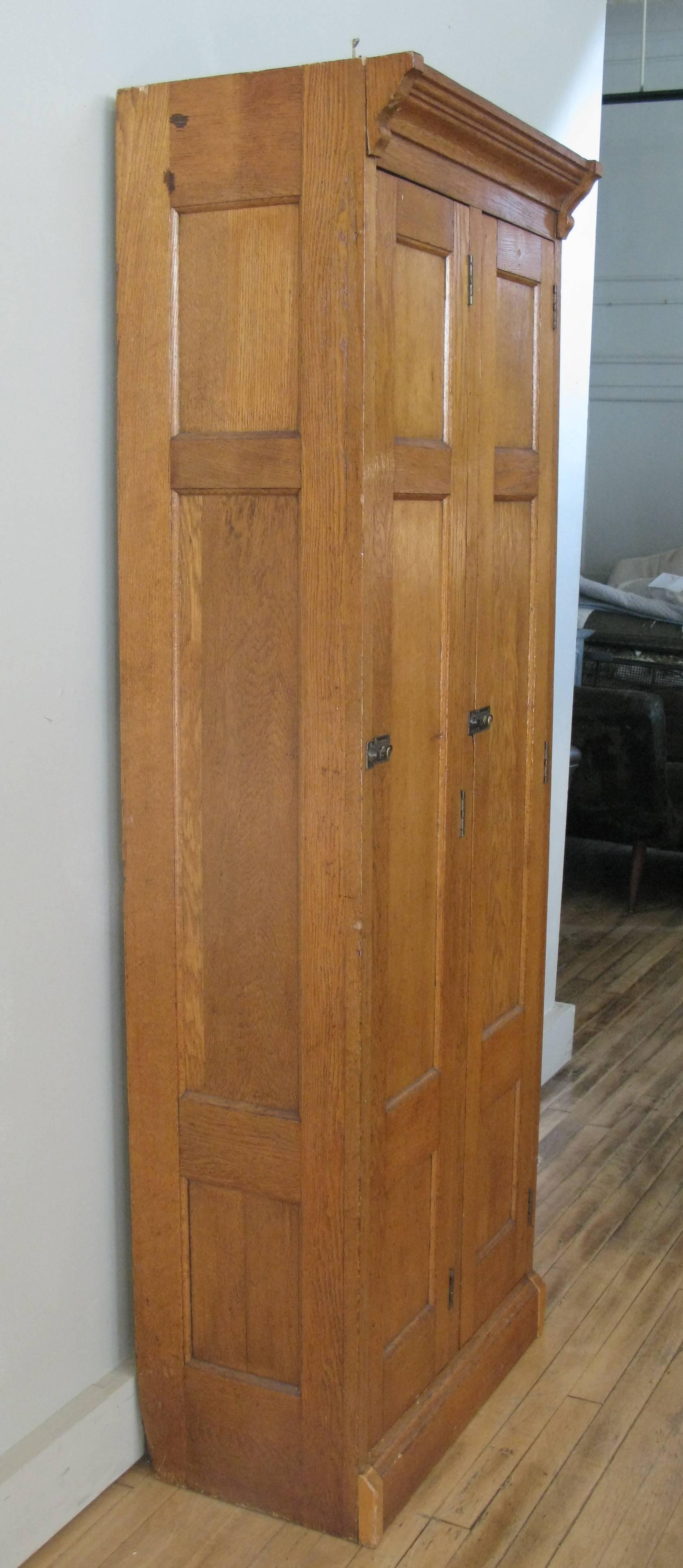 A very handsome antique, 1940s two-door locker cabinet in oak with recessed panels and crown molding. Nice size and scale, each compartment has an upper shelf and three hooks.