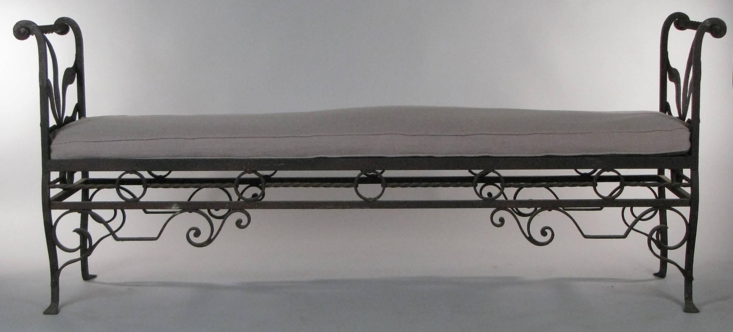 A very well made hand-wrought iron bench, circa 1920, with scroll detail around the base and ends with leaf pattern. Furnished with linen seat cushion.