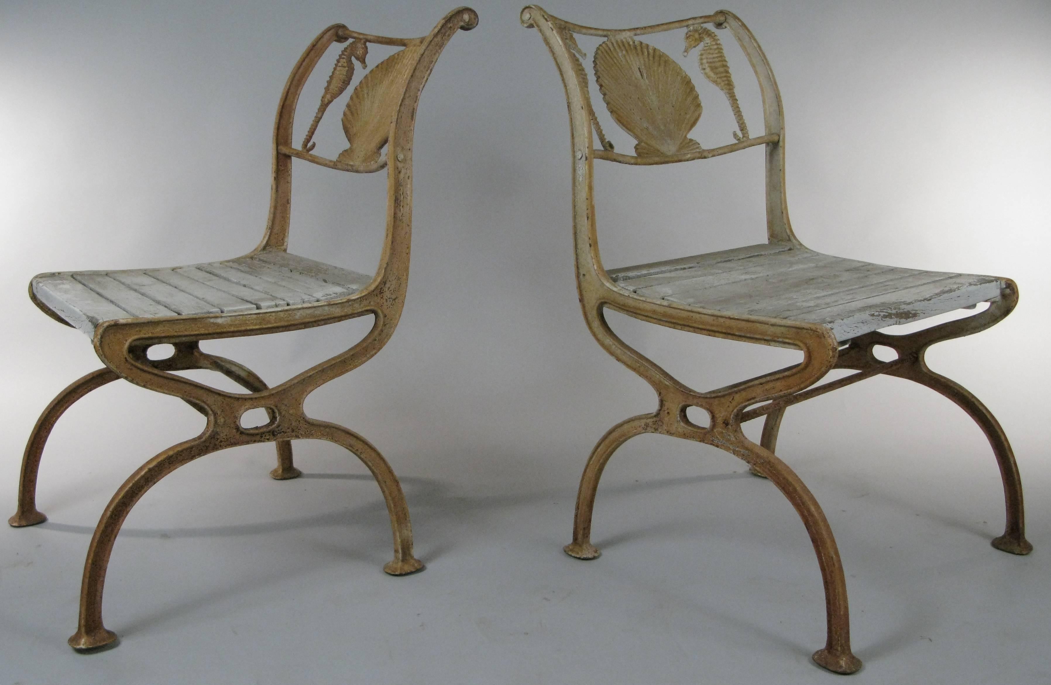 A pair of antique 1920s cast iron chairs with a seashell and seahorse motif in the curved frieze on the back of the chair. This is a rare design and we have four chairs total, priced as pairs.