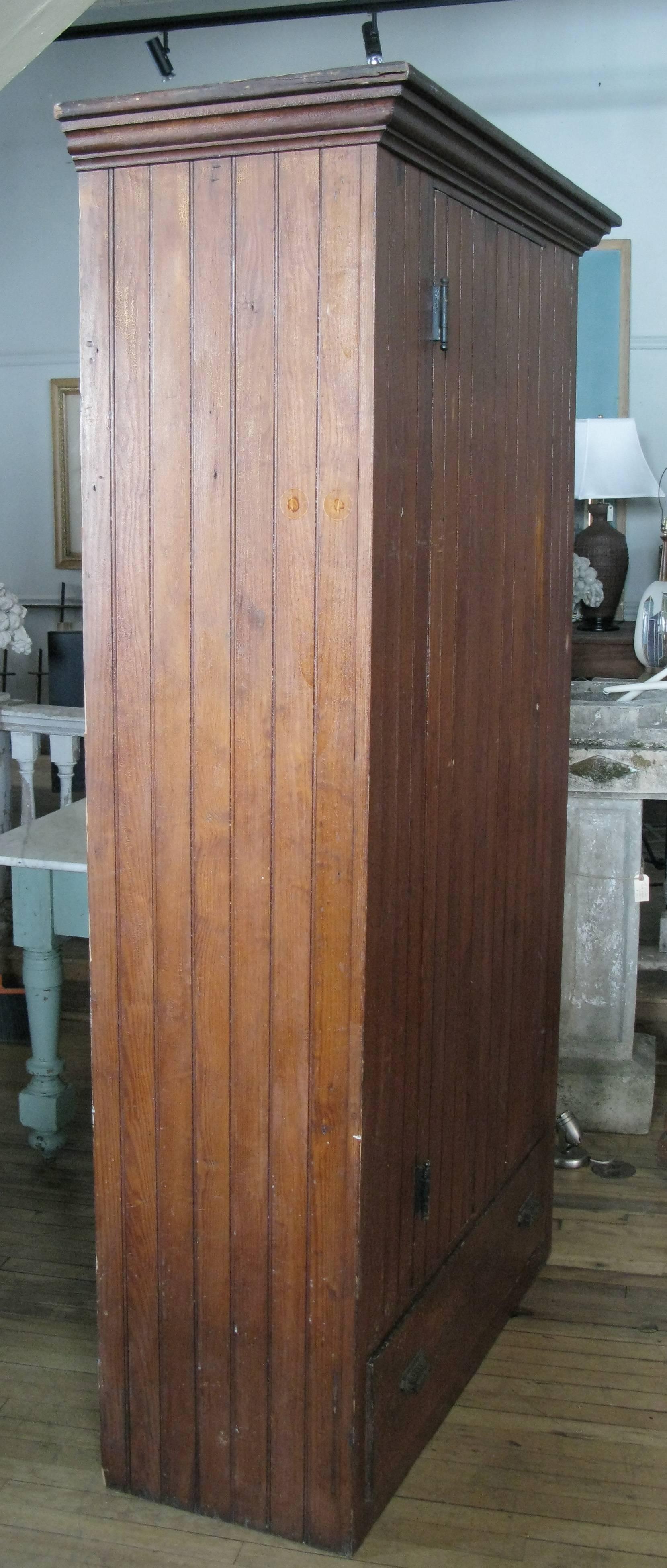 A very handsome antique 1920's tall country cupboard, with oak beadboard construction, a single door with interior hooks and hanging rod, and a lower drawer, in very good original condition.