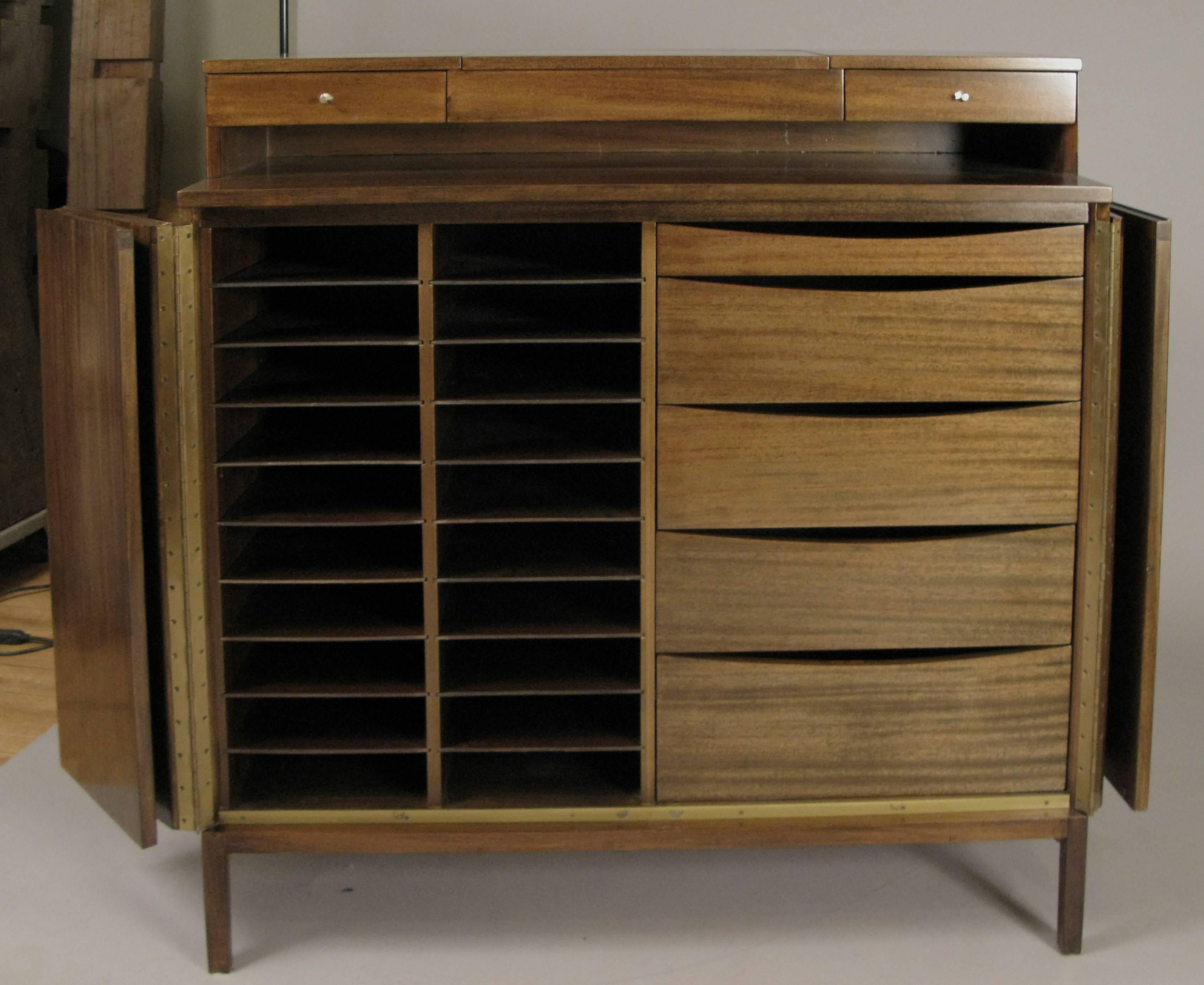 An outstanding vintage 1950s tall gentlemans chest designed by Paul McCobb for Calvin Furniture. The mahogany case has a pair of bi-fold doors concealing a bank of leather lined drawers on the right, and a series of slide out shelves on the left