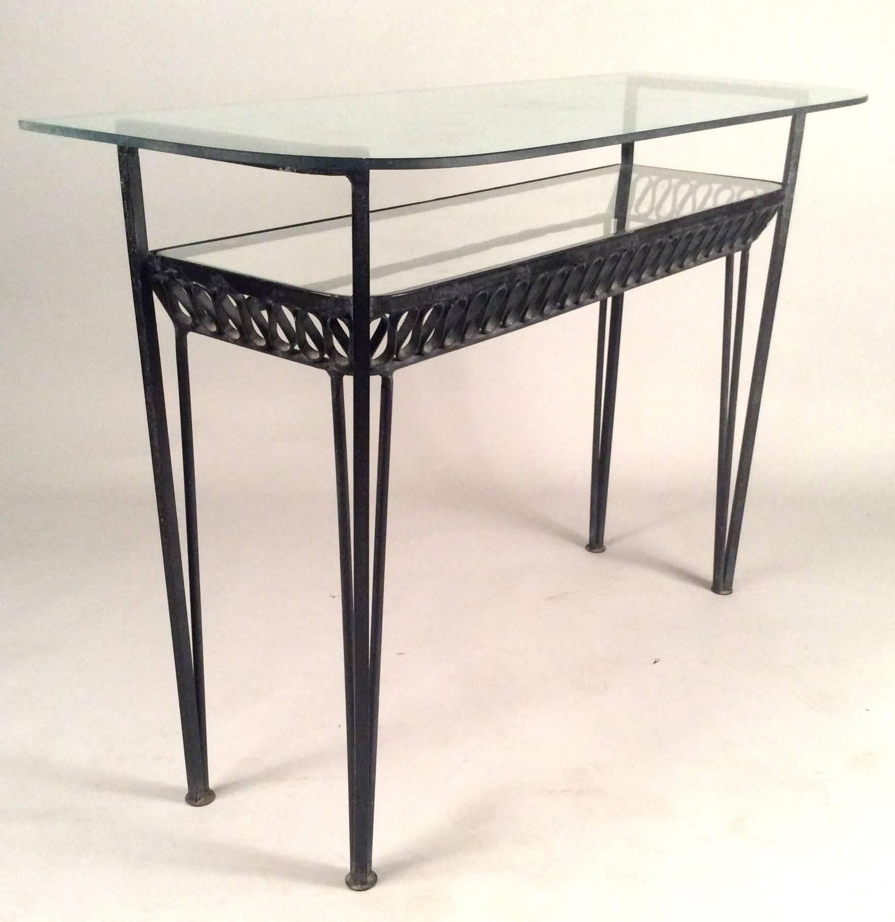 A rare 1950s wrought iron double shelf console table designed by Maurizio Tempestini for Salterini, with two long glass shelves and Tempestini's signature iron ribbon design under the lower shelf.