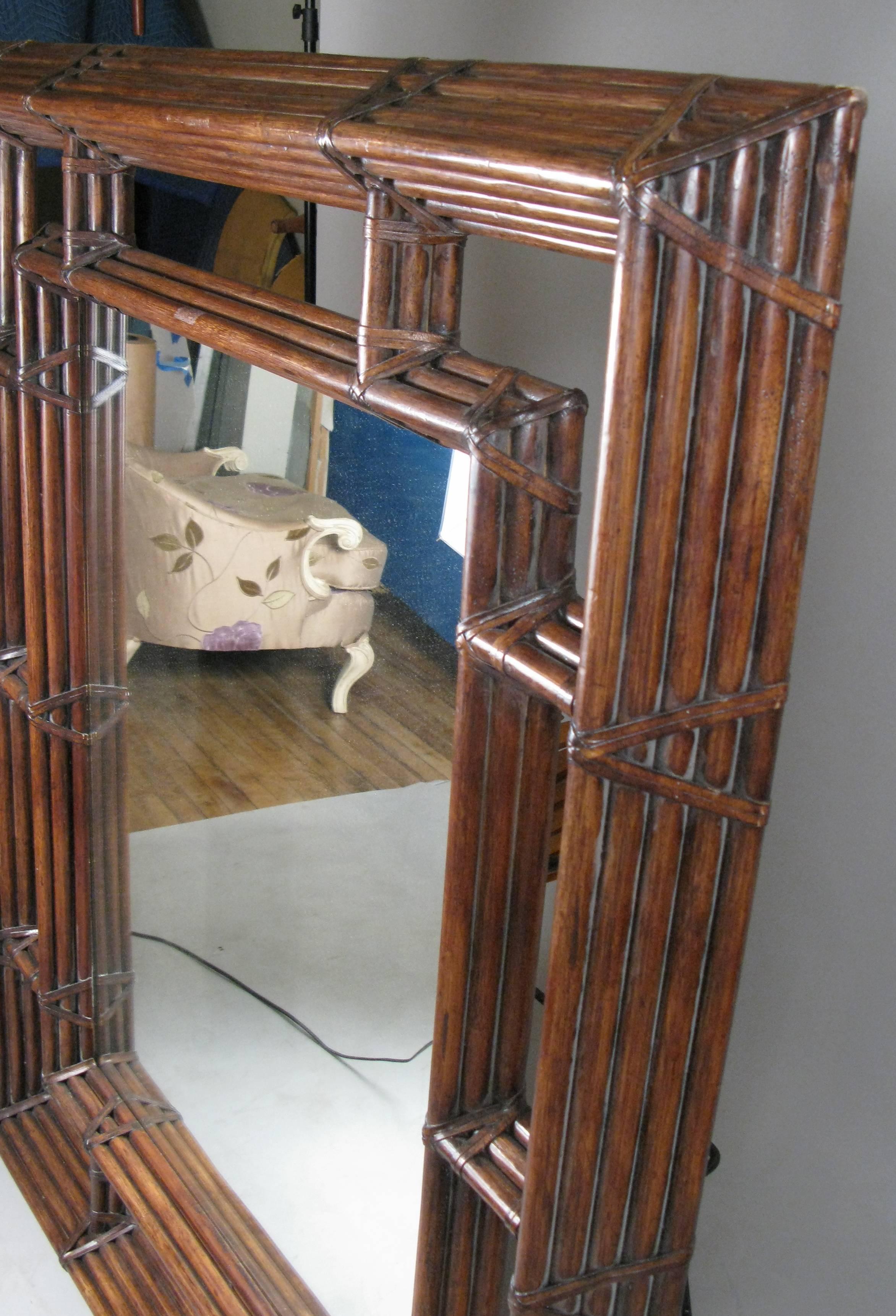 A wonderful large-scale 1970s wall mirror by McGuire, in their Classic and iconic bamboo frame with rawhide lacing. The design features an open outer framework, deeply bevelled, and inner framed mirror, creating an open space between the two frames.