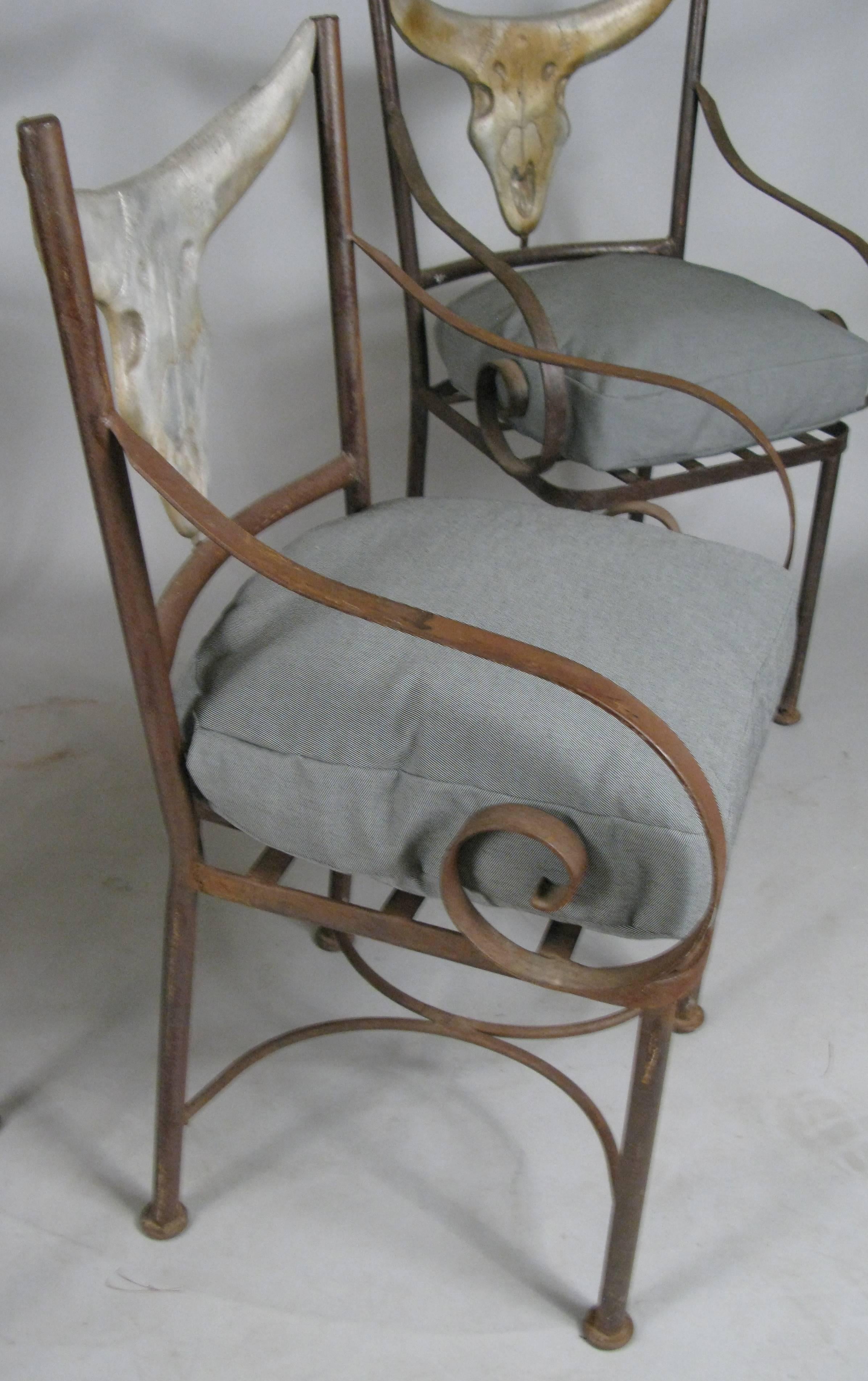 A very handsome set of four iron chairs with scroll arms and back in the cast form of a steer head. Very well made and unique. With new seat cushions in grey all weather fabric.