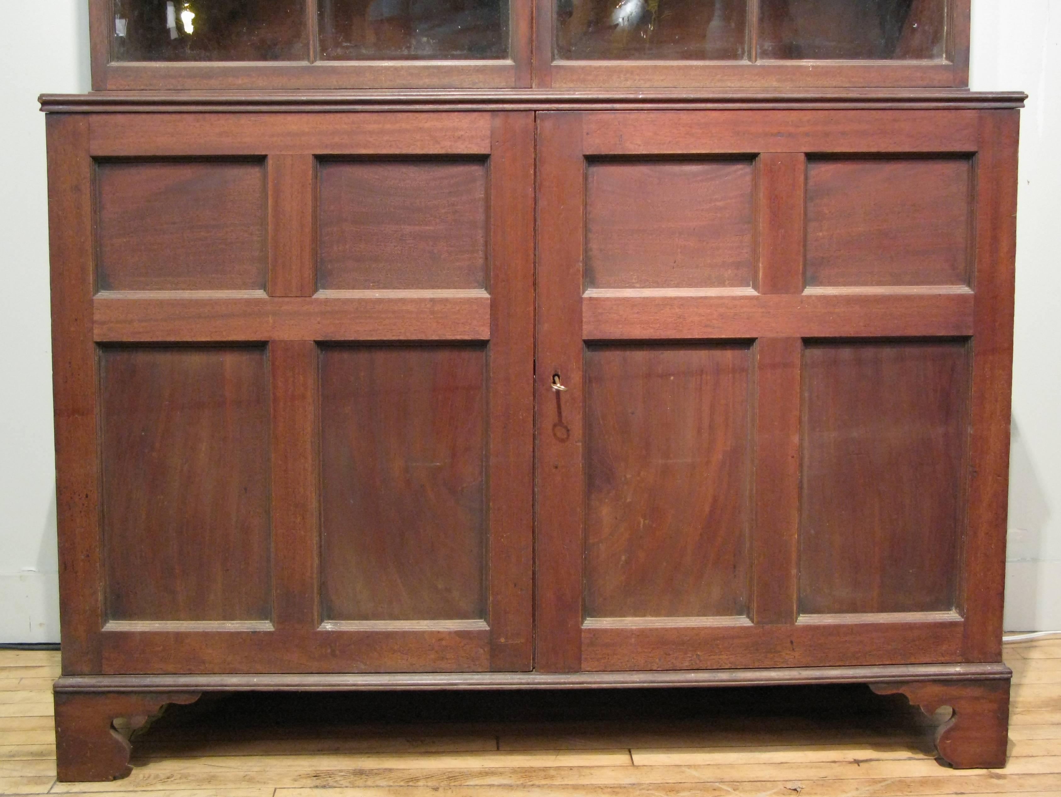A very handsome antique late 18th century mahogany cabinet, with a base with hinged doors and a divided interior. The upper portion has a pair of hinged doors with original glass and very slim mullions and a divided interior. This is a very