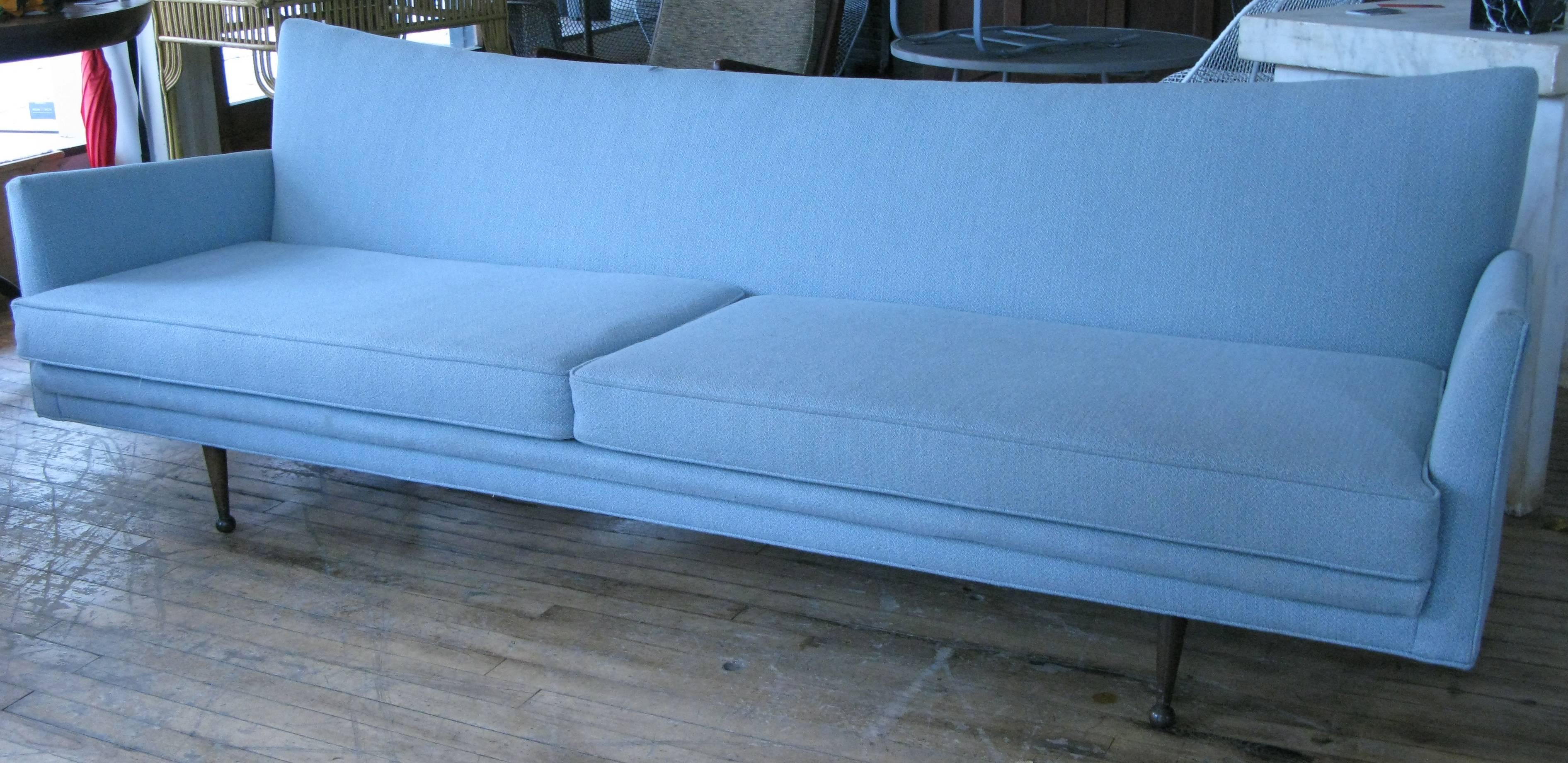A very handsome 1950s modern sofa, with slightly raised tips on the wingback, and raised on tapered walnut legs. In original powder blue upholstery.