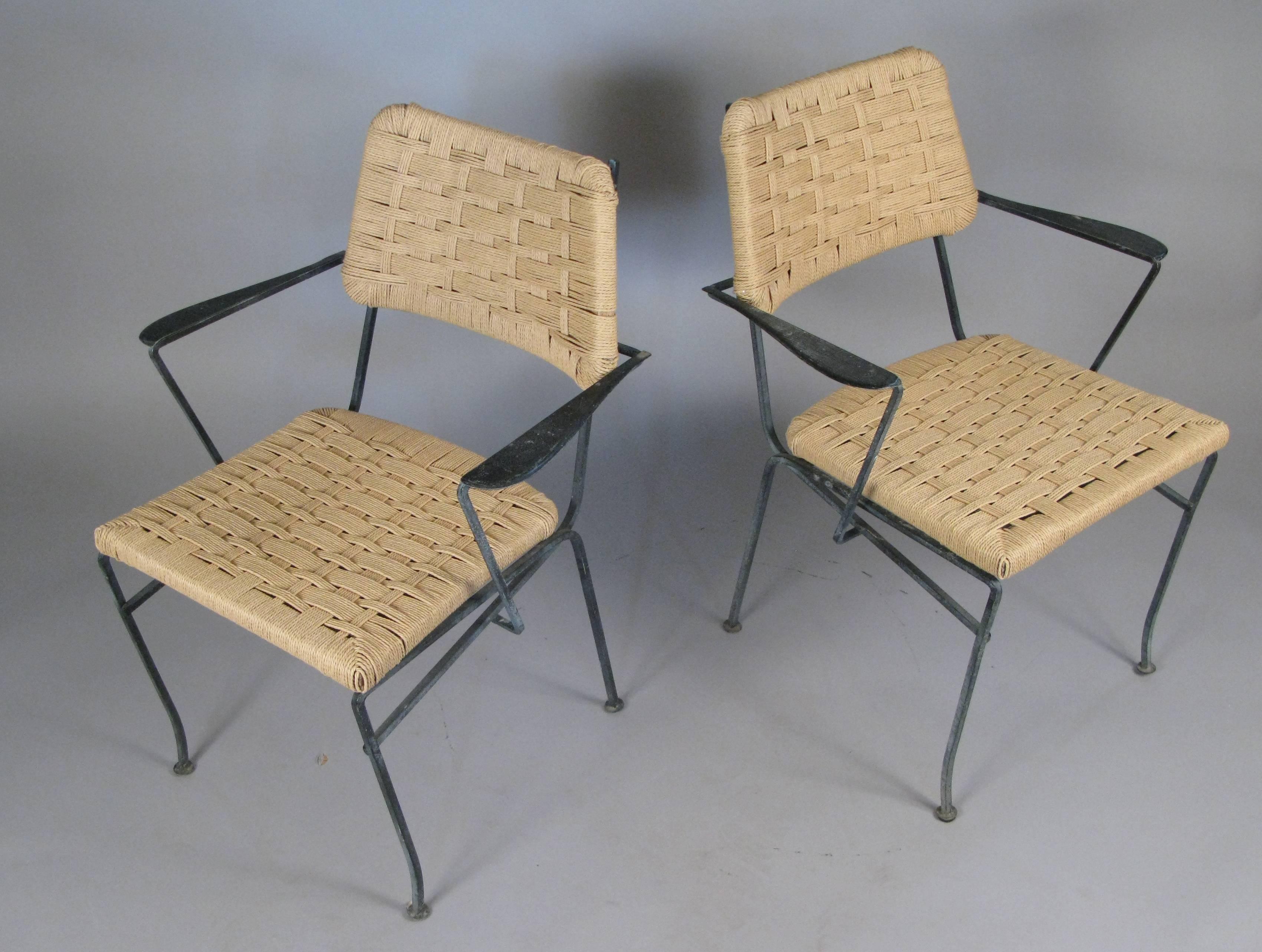 A pair of 1950s wrought iron armchairs by Salterini with beautifully made iron frames. Seats and curved backs are covered in woven rope cord over wood frames. Elegant design and very comfortable. All of the woven cord has been expertly replaced.