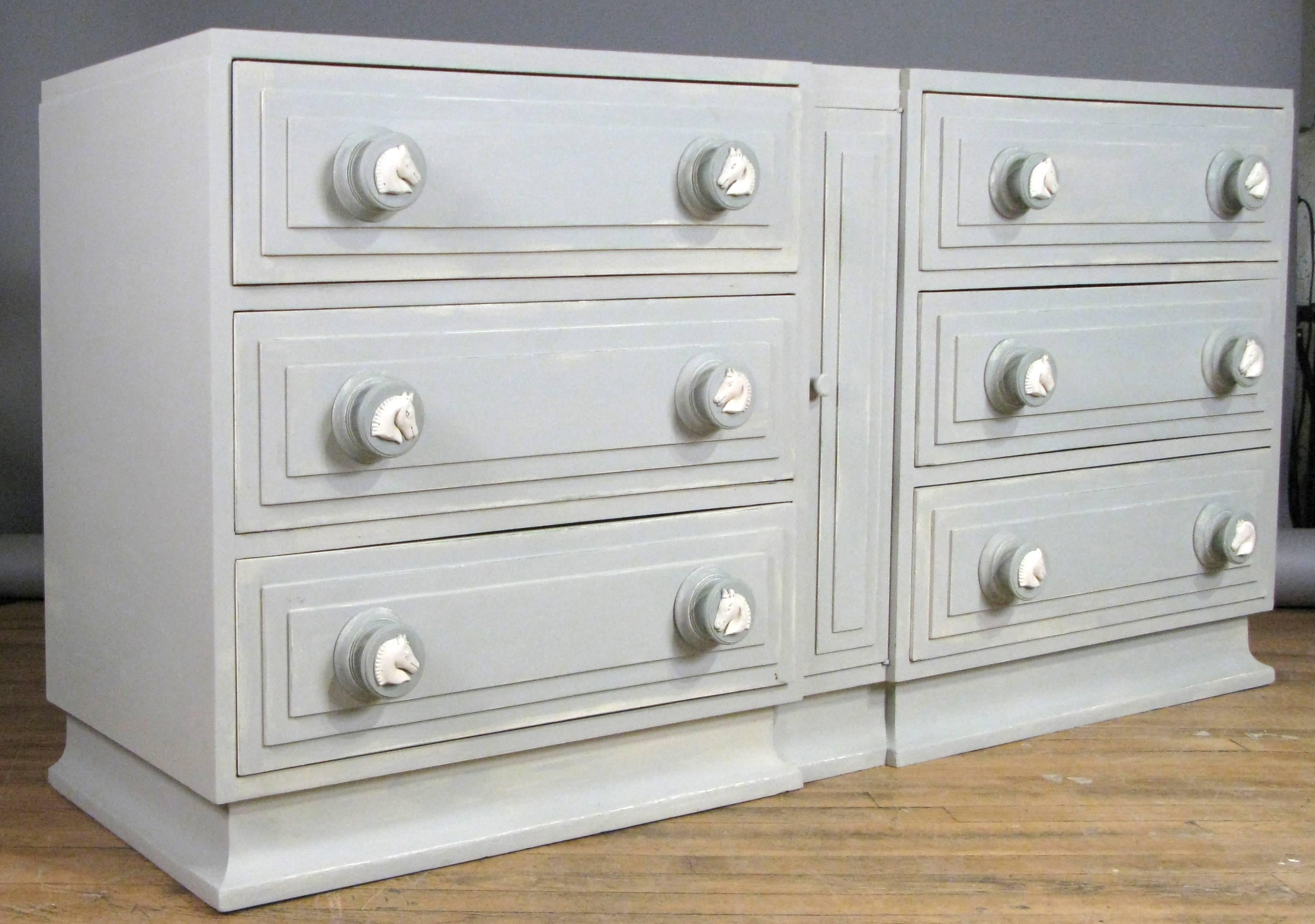 A very handsome 1950s six-drawer chest by Maslow Freen with carved wood horse head details on the drawer pulls and an ogee base. This chest has been hand-painted in a pale grey with medium grey accents. There is a tall vertical door in the centre as