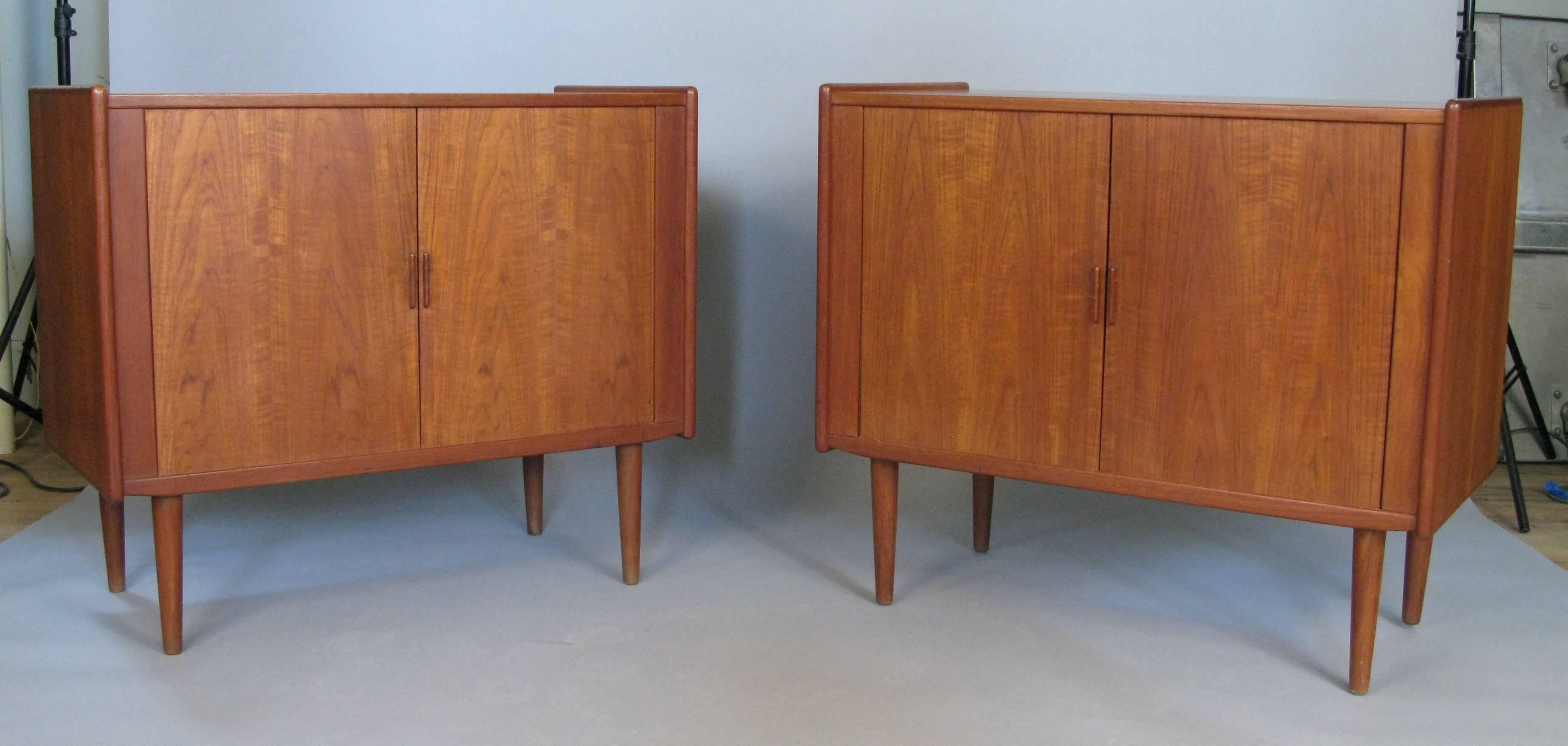 A beautiful matched pair of 1950s Danish teak cabinets with tambour doors and adjustable shelves. Nice scale and design with subtle details. Raised on tapered teak legs.
