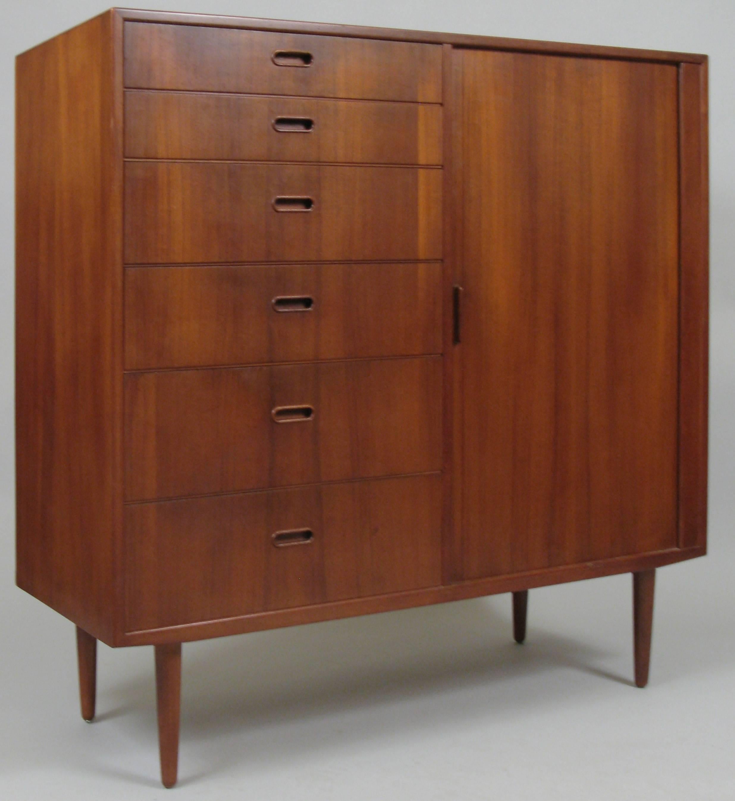 A very handsome vintage Danish teak tall gentlemans chest with a tambour door on the right side of the case concealing six drawers and six graduated drawers on the left side of the case. Beautifully grained teak in this generously scaled storage