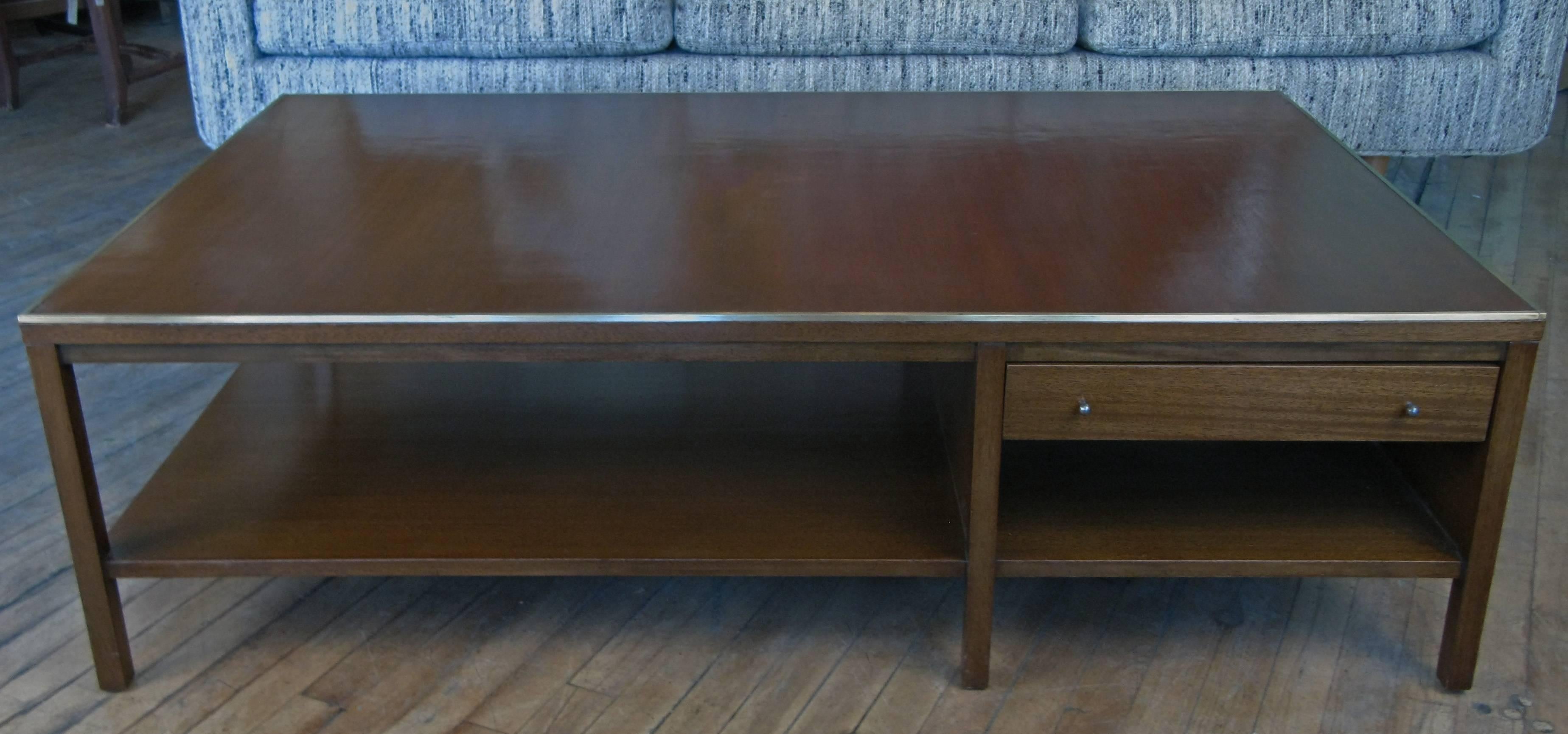 A large and elegant vintage 1950s coffee table in mahogany with a lacquered leather top and brass trim. Very nice scale and proportions, with a lower shelf and a single drawer. Labelled Paul McCobb for Calvin.
