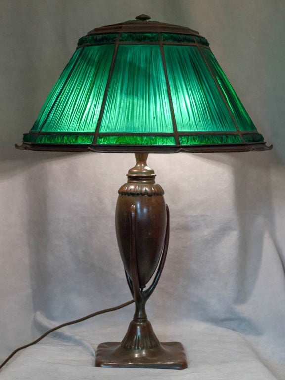 A very fine example of a Tiffany Linenfold lamp. These usually come in gold glass. The green glass is more desirable and much more beautiful. The bronze base is referred to as the 
