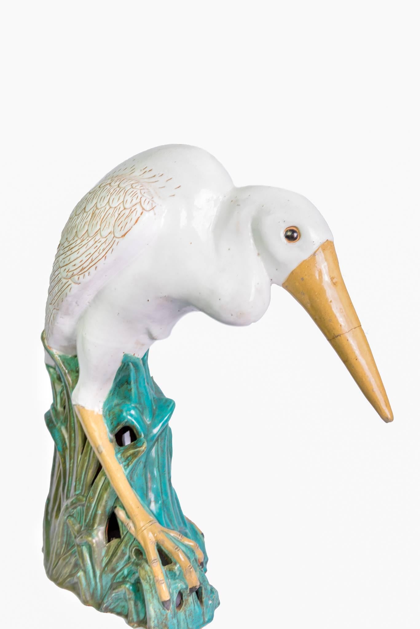 Glazed ceramic herons in the French Colonial style depicted as if they were standing in water with water plants at their feet.