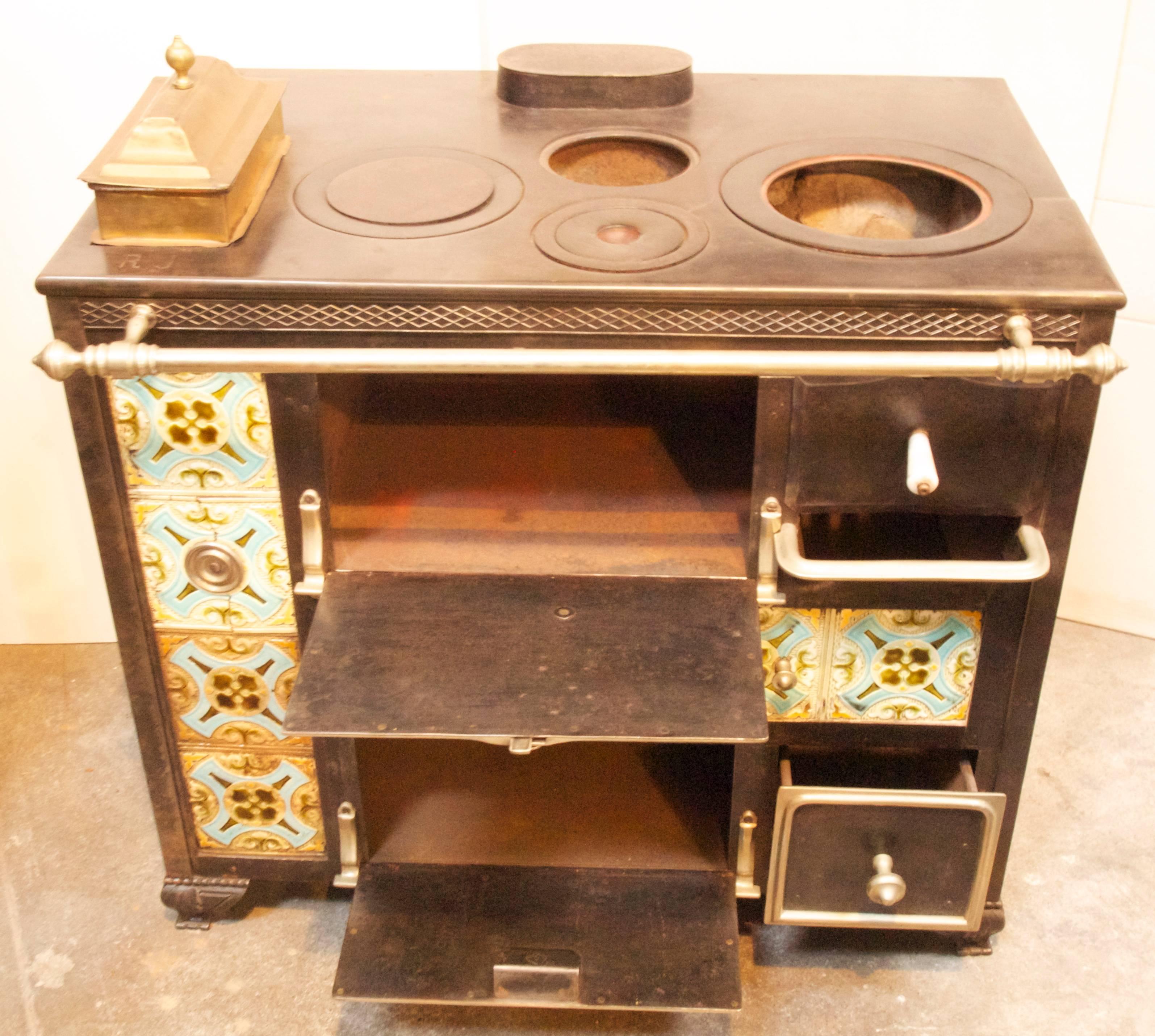 Early 19th century French coal and wood burning cast iron cooking stove with nickel plated hardware, brass and ceramic tile decoration.