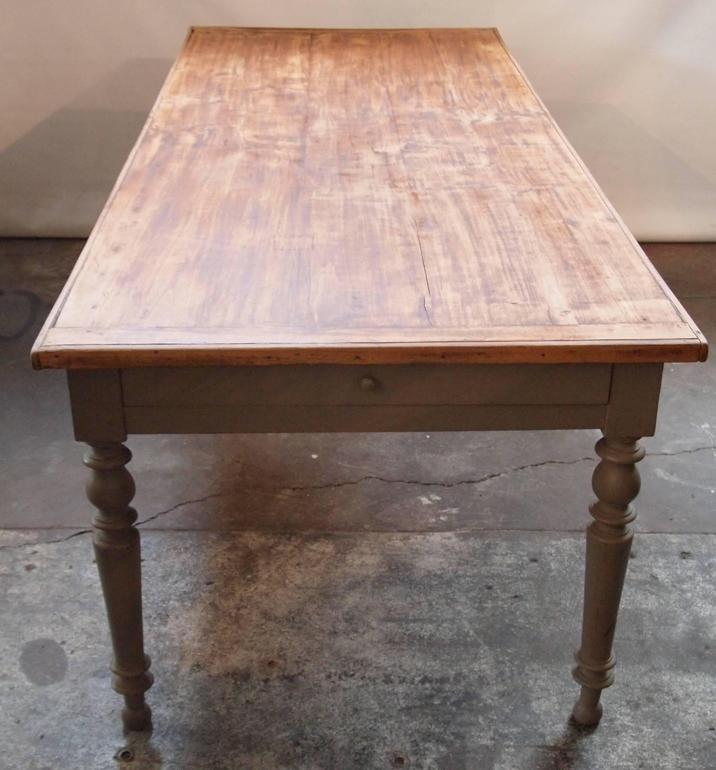 Provincial French farm table with a stained pine wood top on a grey painted base with turned legs. One drawer and one slide at each end.
