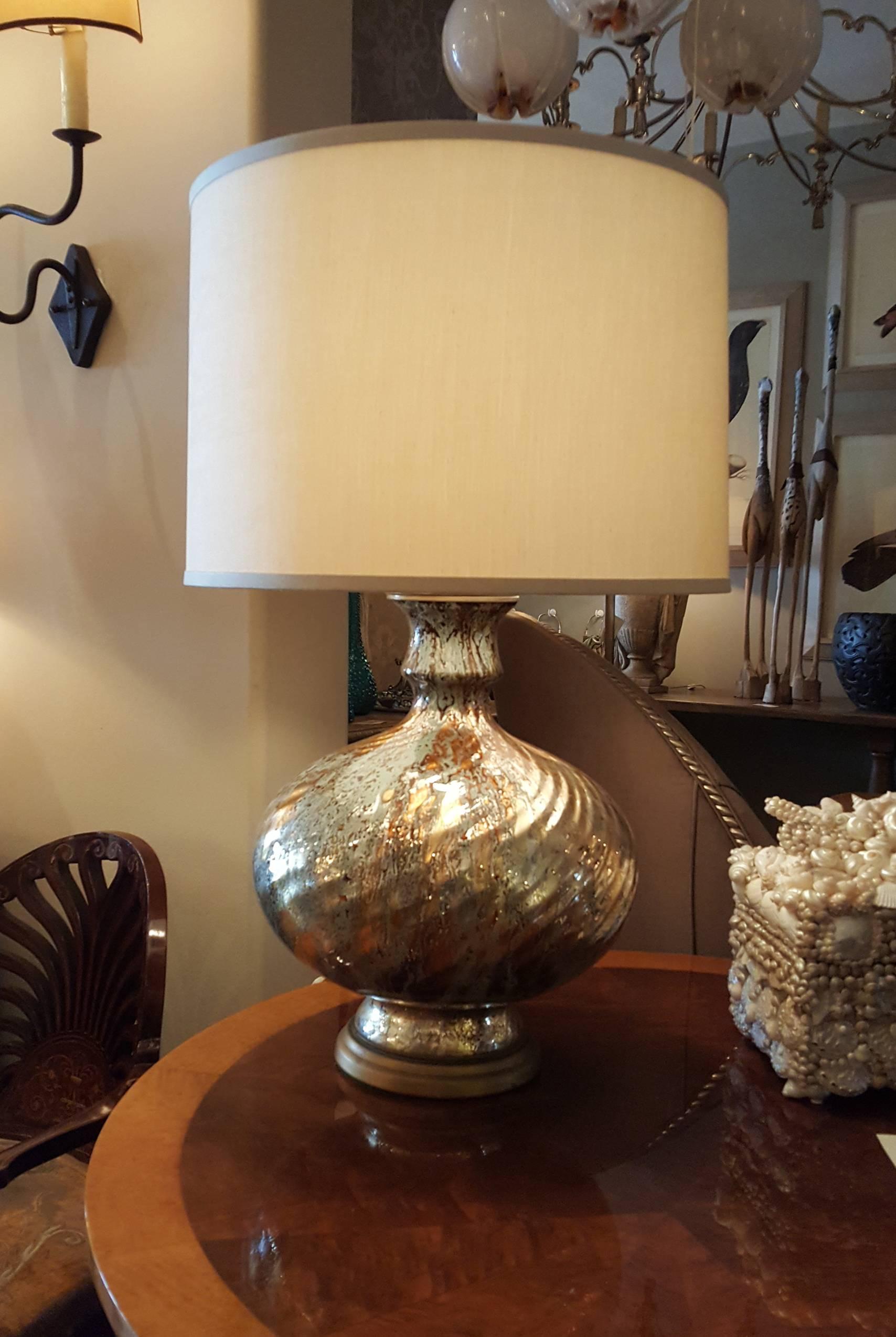 Generously proportioned mercury glass lamp with swirled base and new silk shade. Gold and copper colors exist in the mercury glass. Gold colored base. Believed to be from the 1960s. 

Measures: Shade top diameter: 19