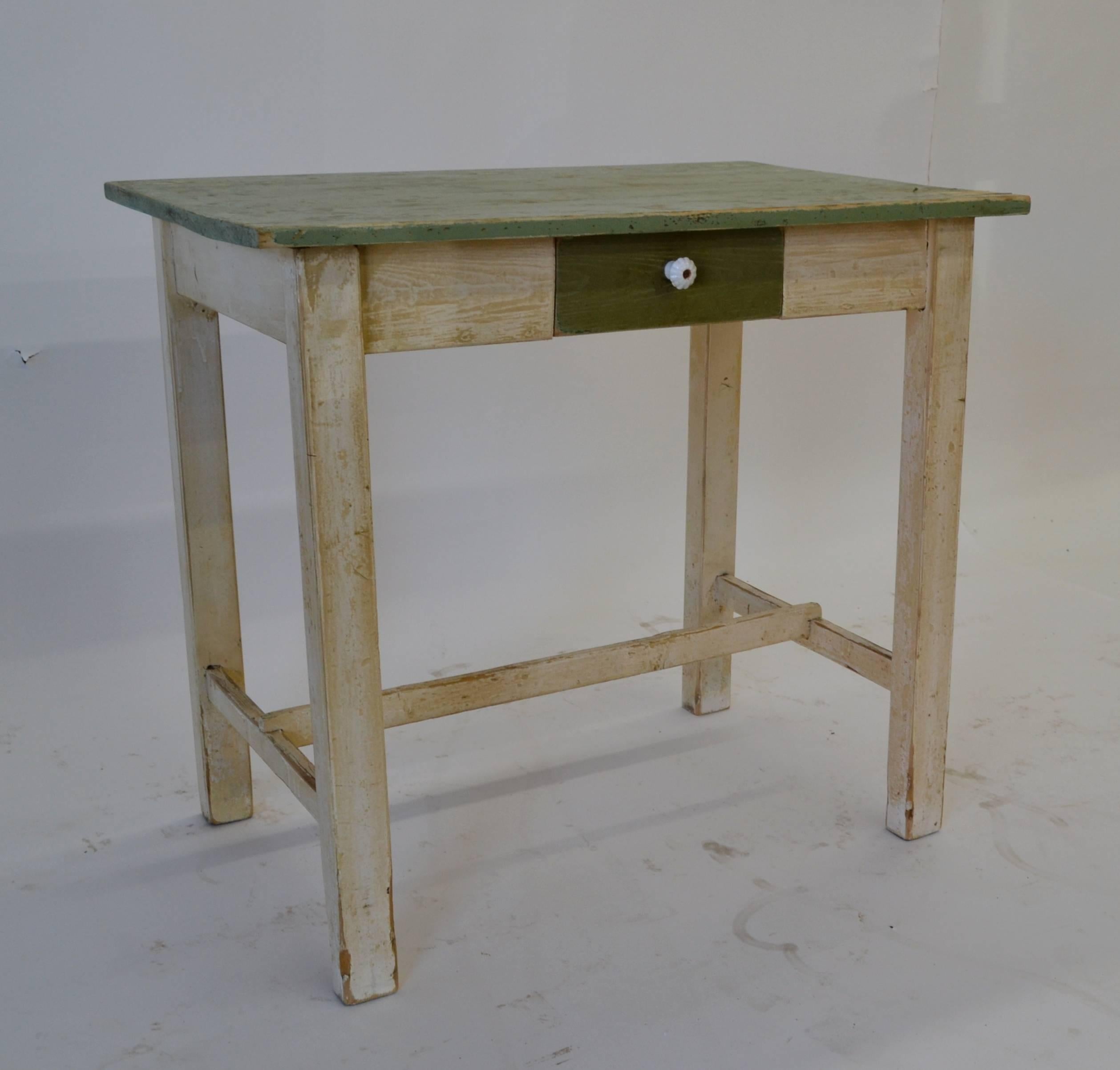 A small pine table with a single central hand-cut dovetailed drawer on straight legs joined by a central stretcher. In old worn green and off-white paint.