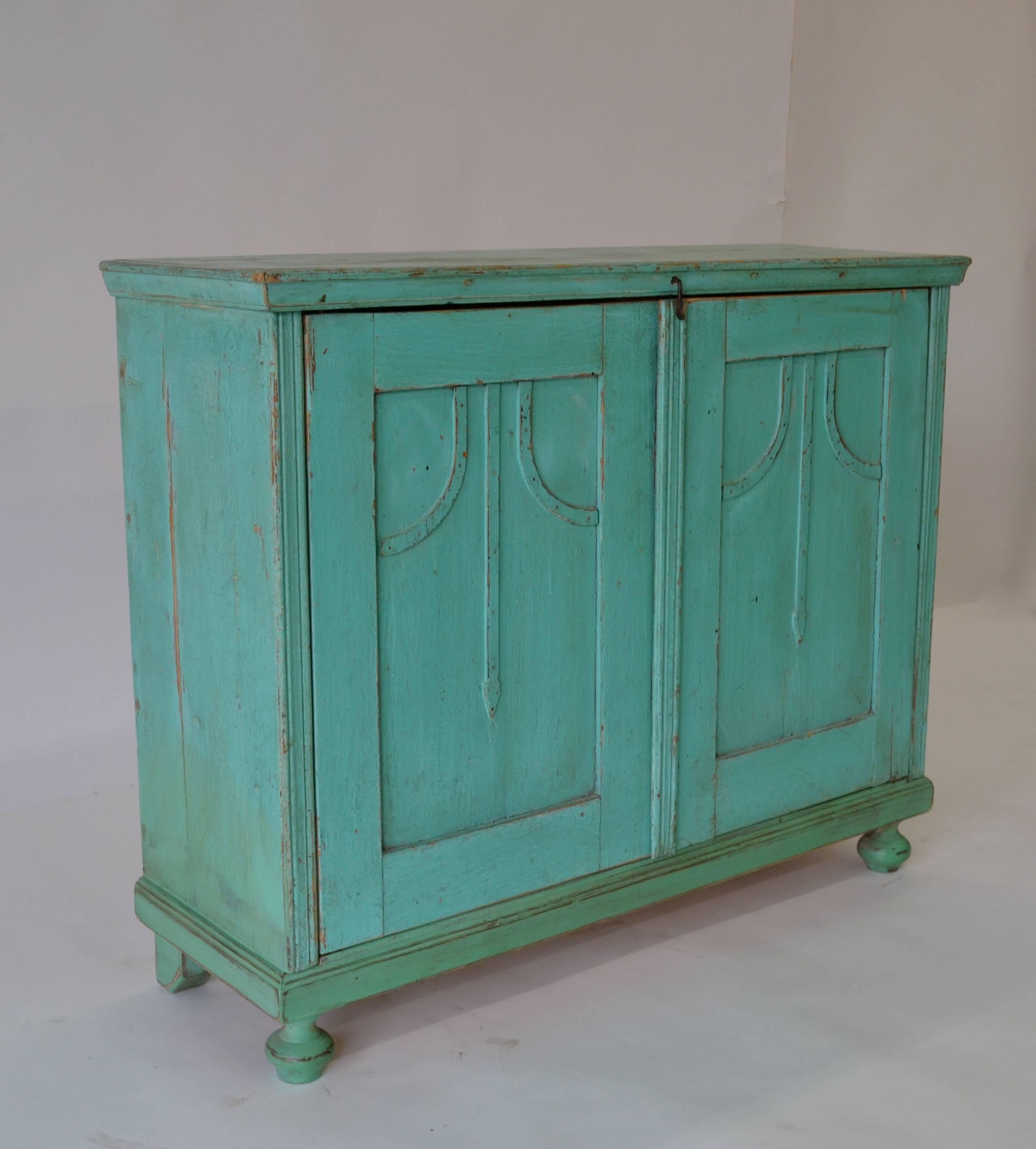 A small two-door pine cupboard with applied with arts and crafts style mouldings to the paneled doors. The shallow profile of this piece makes it useful for storage anywhere. In old worn bright aqua blue paint.
