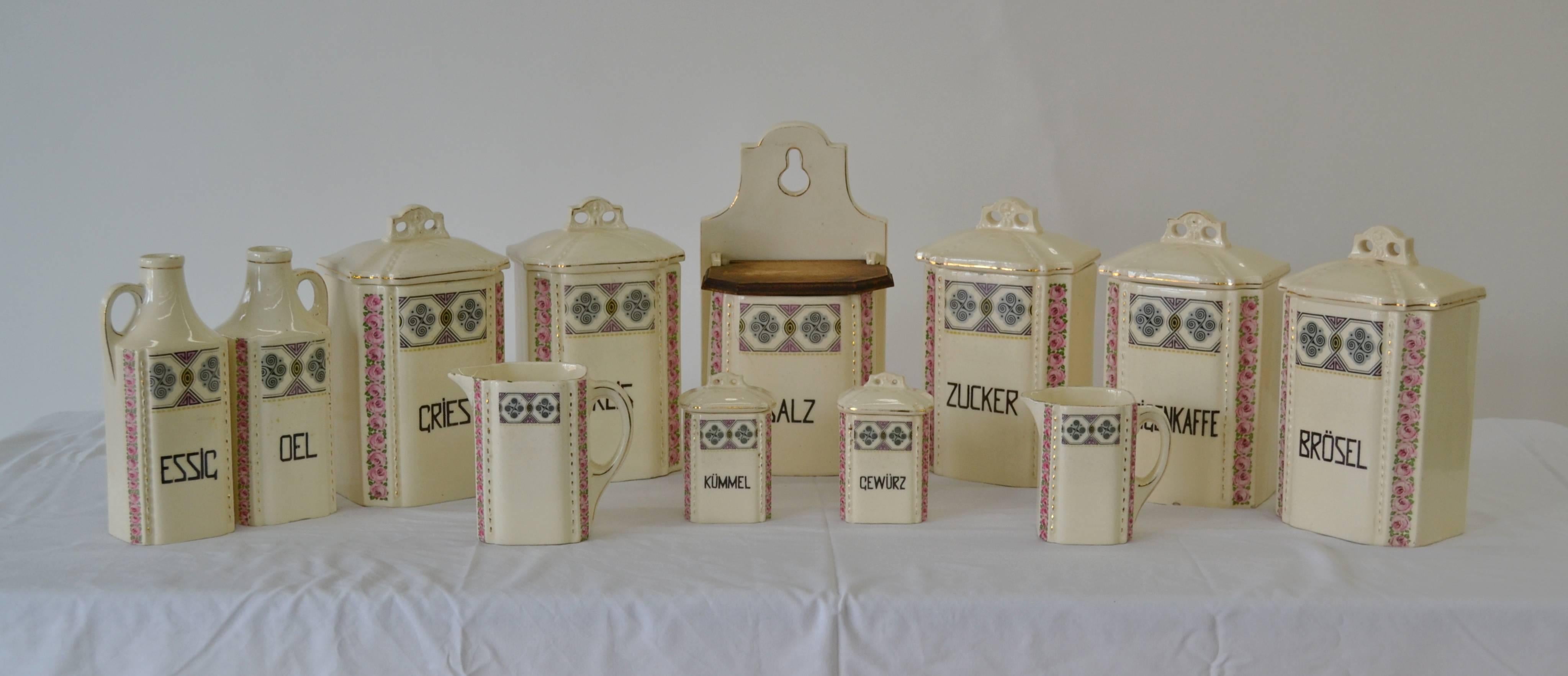 A vintage set of porcelain Art Deco kitchen canisters by Gretl of Czechoslovakia, with a geometric pattern transfer on the front and a flute of pink roses on the front corners. Comprised of 12 pieces including a hanging salt box with wooden lid and