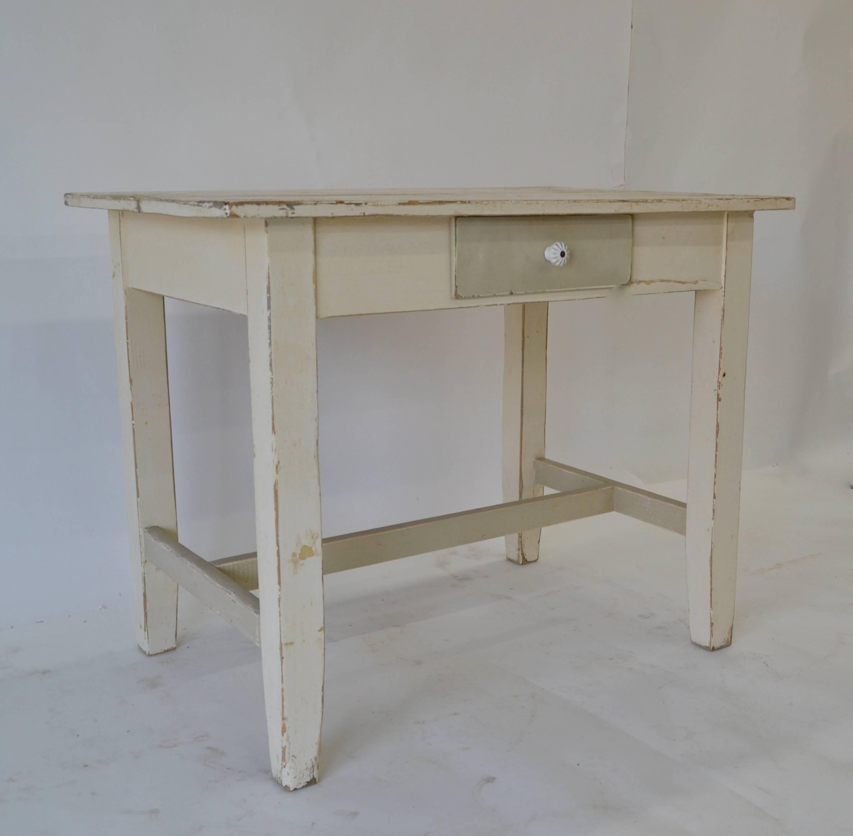 This is a small pine stretcher base table with a single hand-cut dovetailed drawer. The square legs taper slightly towards the foot. Great in a small kitchen or as a writing desk. In old worn Gustavian-like tones of grey and white paint, with much