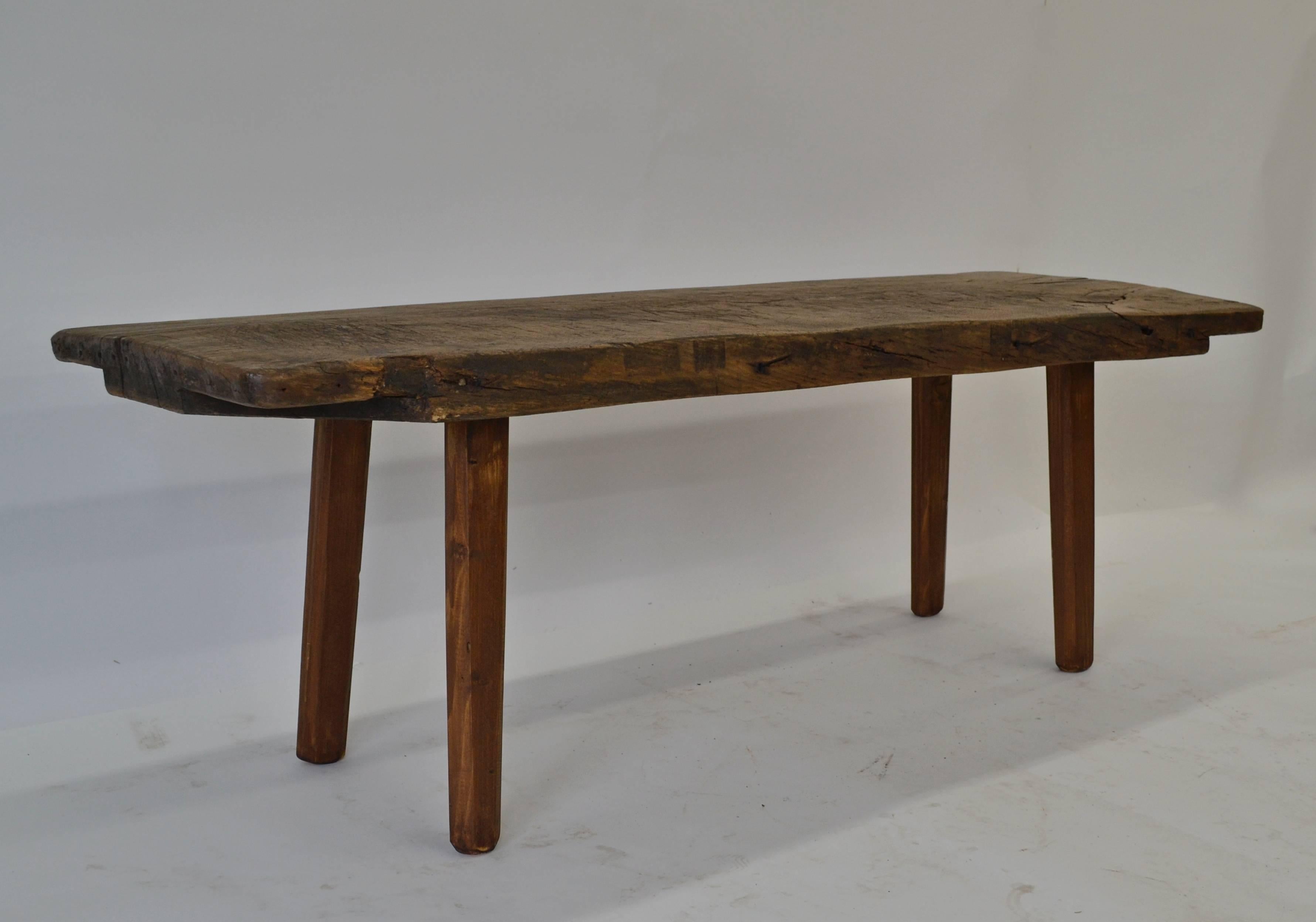 This is a marvelously scored, gnarled and beaten up antique pig bench with a 2.5” thick oak top, cut to 20” high for use as a coffee table or low table for plants or as an entryway or mudroom bench for taking off boots and popping them underneath