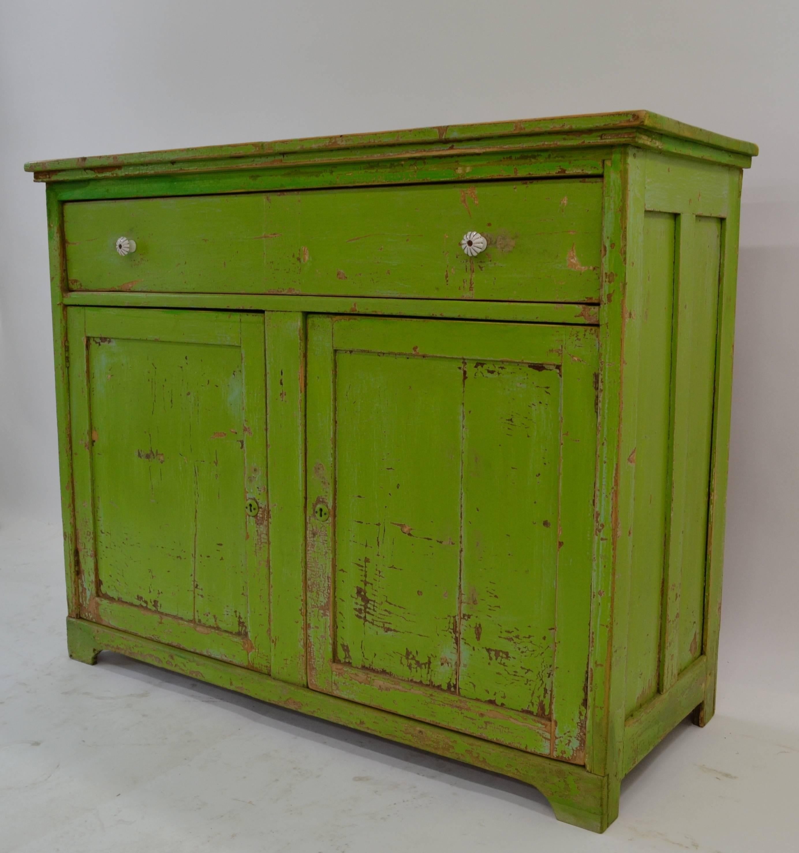 A splendid piece of plain country furniture, this large dresser base with paneled sides features a single deep full span dovetailed drawer above two paneled doors separated by a central stile. The interior has a single original shelf. In shades of