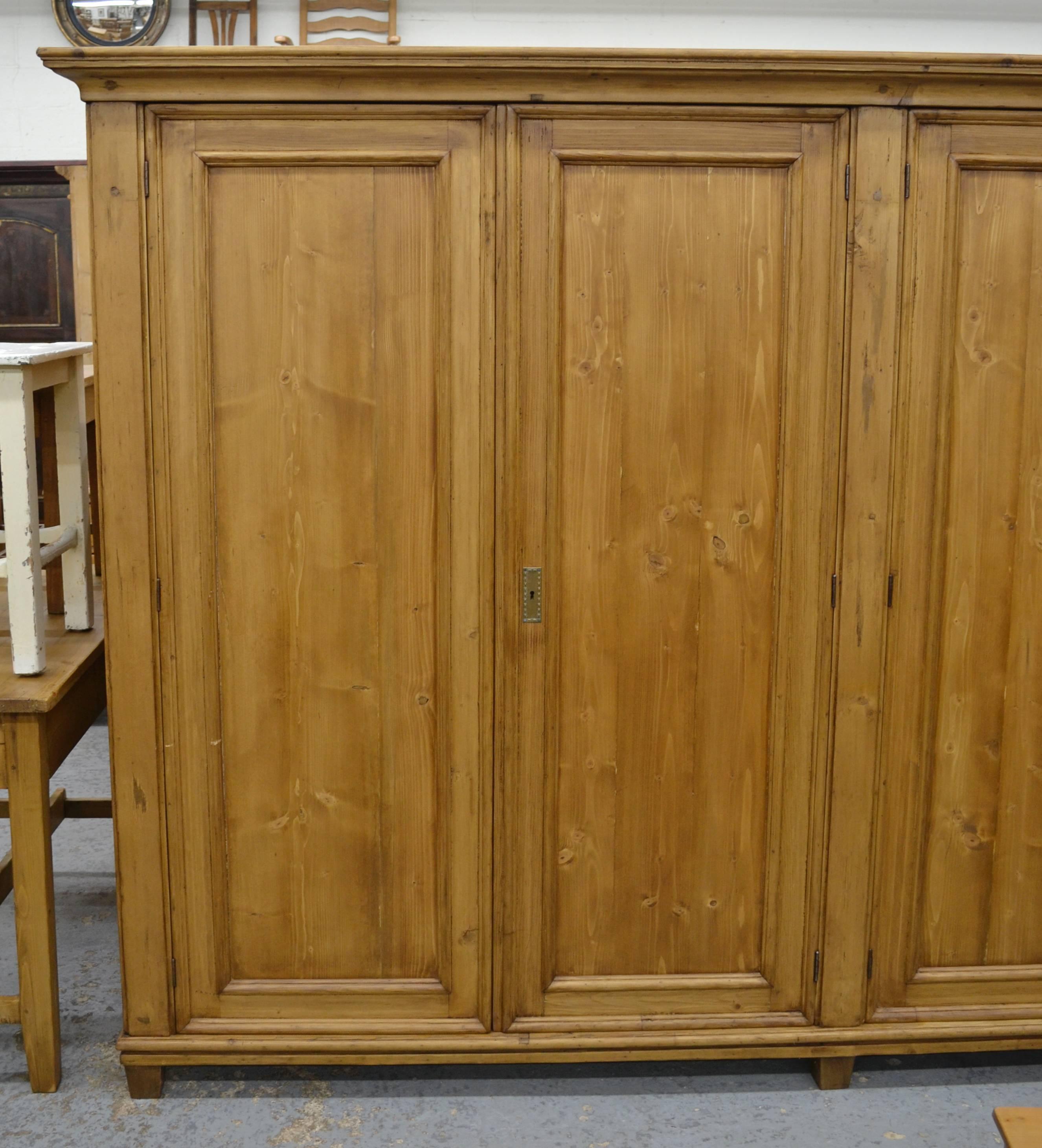 Give this four-door wardrobe a wall ten feet long and it will take care of all of your storage needs. Once a glazed display cabinet, this piece lost its glass and has been restored with panels from reclaimed pine. A bold crown sits above four