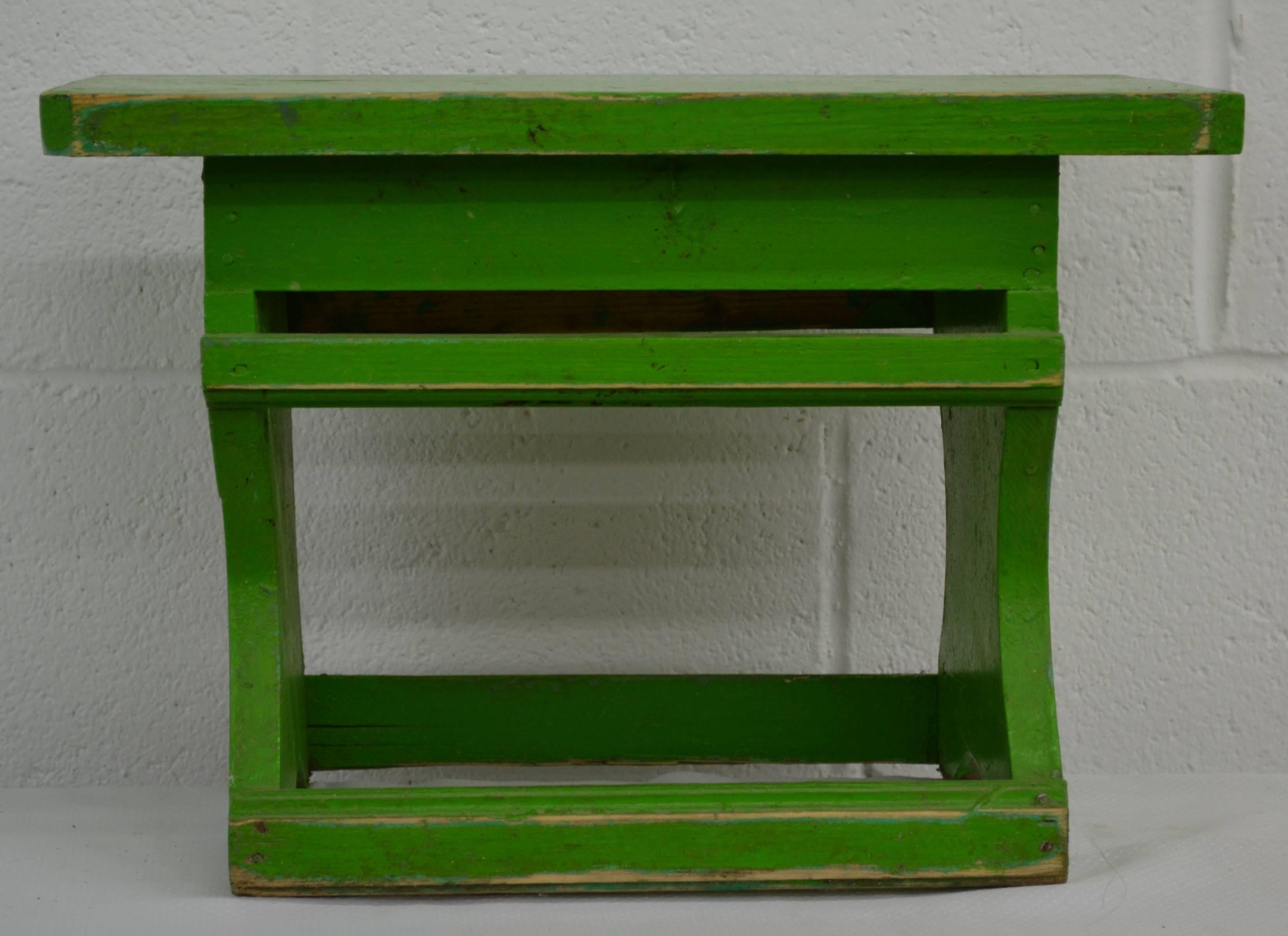 Ein großer und stabiler Fußschemel aus Kiefernholz mit ebenem Boden und seitlichen Läufern, in alter, grüner Farbe.  
