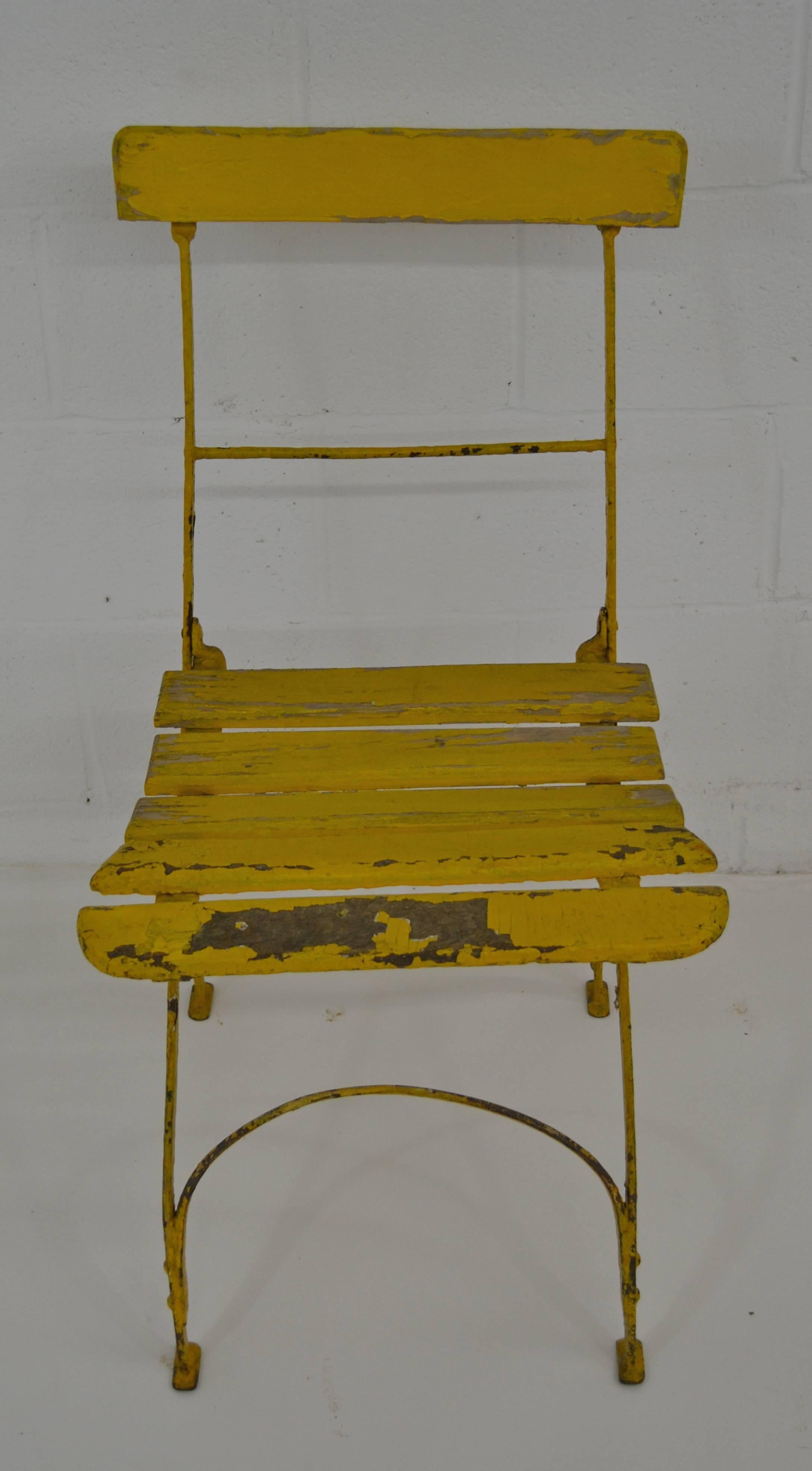 A single vintage wrought iron folding bistro chair with oak back rail and seat slats.  In original very worn yellow paint.

