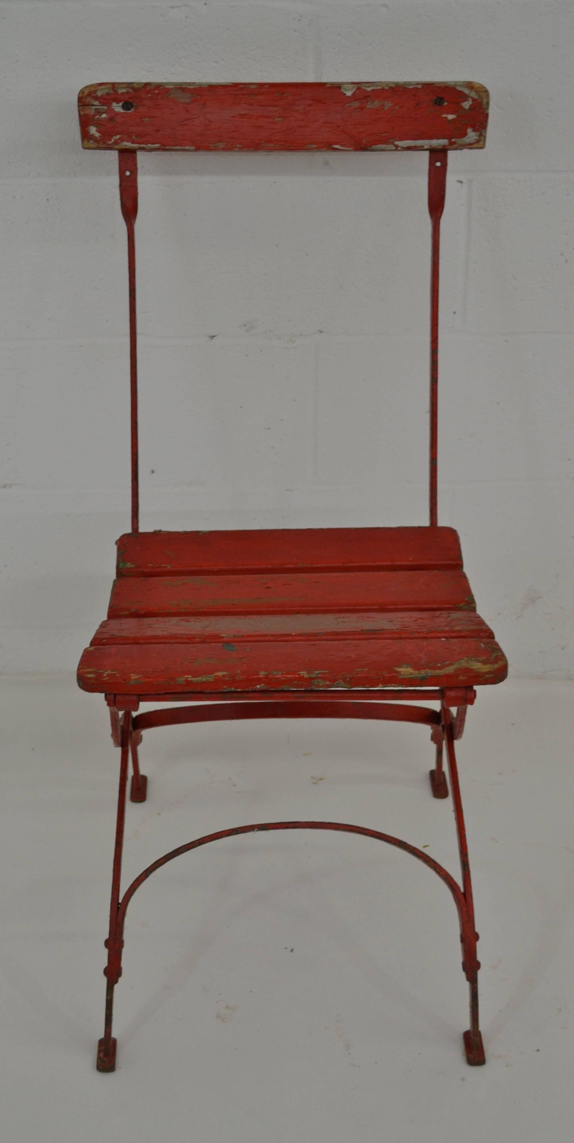 A wrought iron folding bistro chair with oak back rail and seat slats. In old very worn red paint on original green.