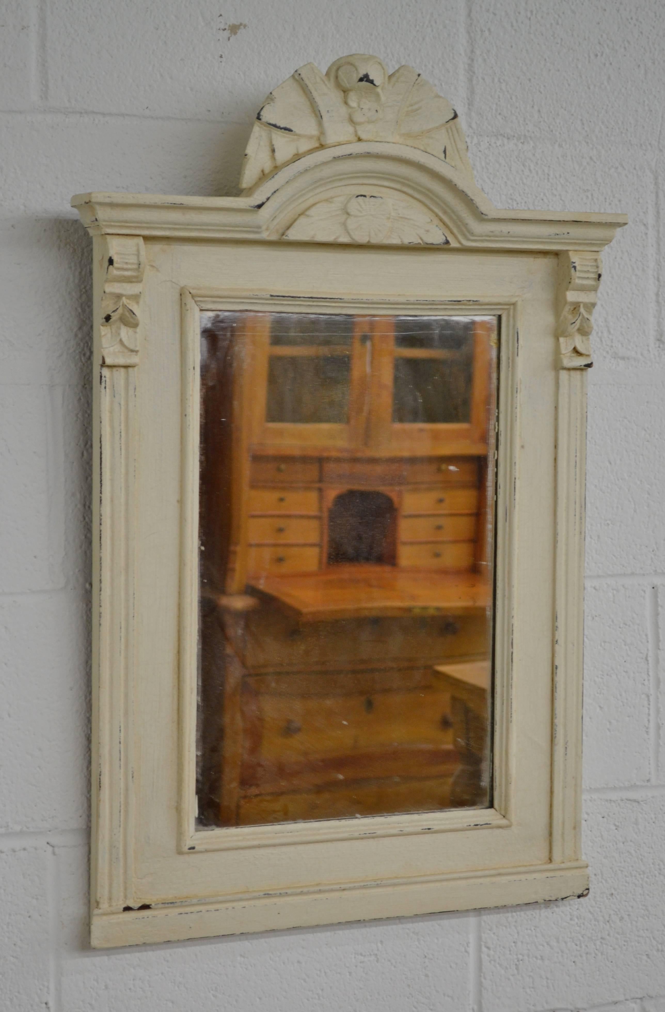 An antique pine frame with fluted molding and acorn corbels to the sides and an arched crown with a carved floral cartouche, fitted with new mirror glass. In old worn and crackled cream-coloured paint.
 