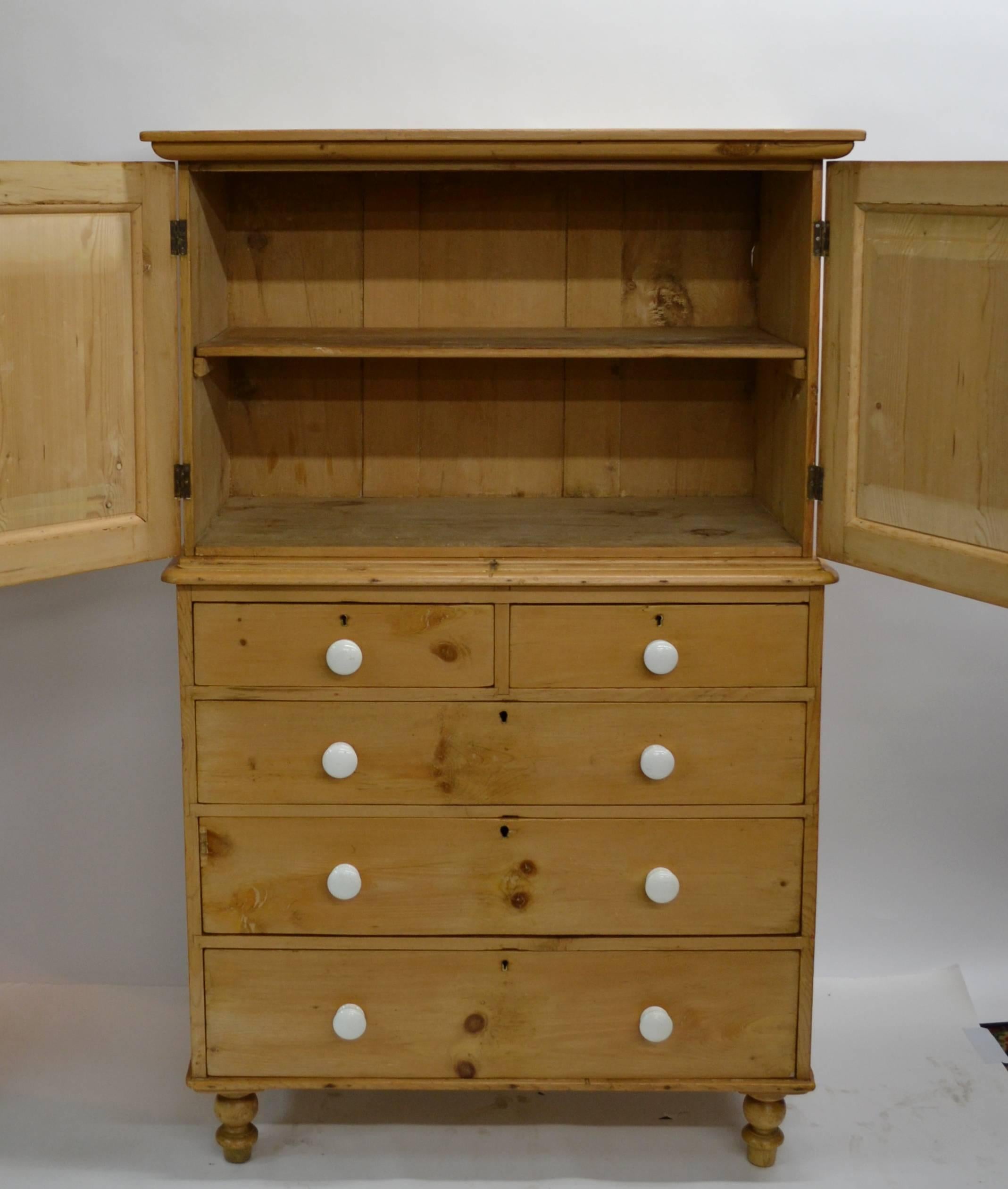 Rather like a diminutive linen press, this is a lovely little English pine cupboard on chest, built in two pieces.  The upper section has a bold but simple crown and two wide-swinging paneled doors with replaced ceramic knobs, which open to a