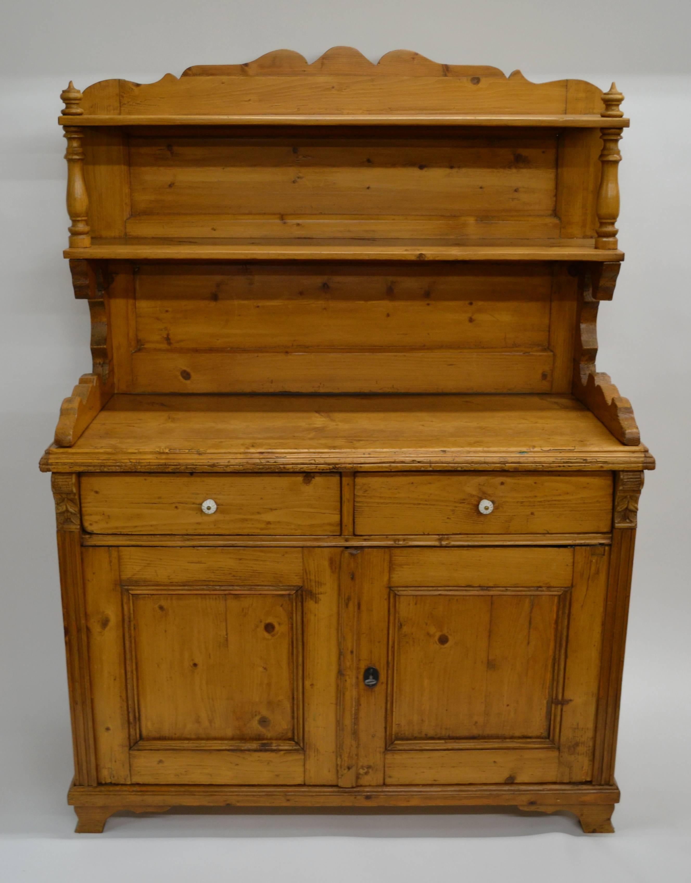 A very rustic and gnarled pine chiffonier, the base with two hand-cut dovetailed drawers above two paneled doors flanked with fluting and acorn corbels. The deep work surface is mounted by a two tier open rack with scalloped side supports beneath a