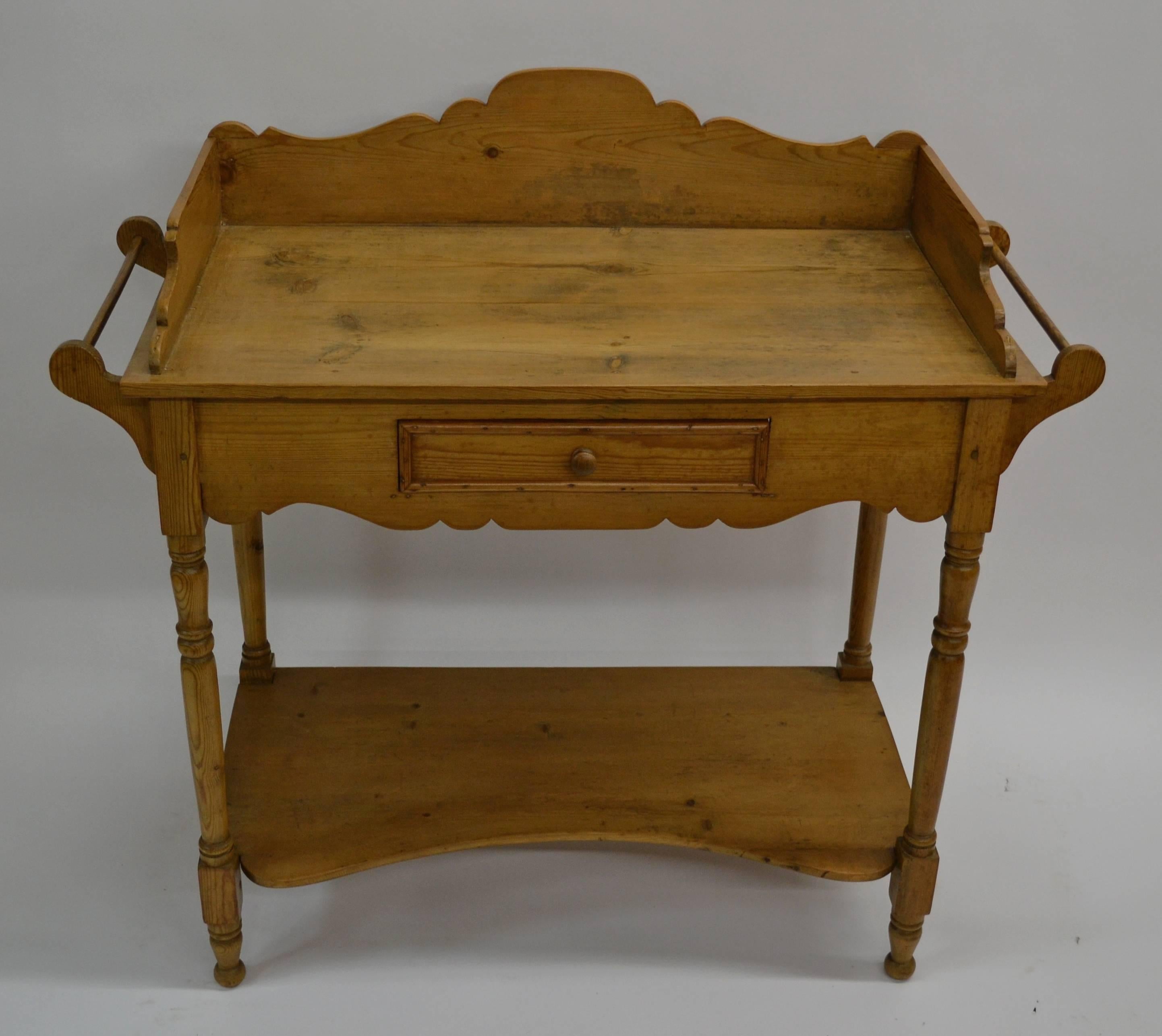 A Classic English pine turned leg washstand with a scallop-fronted potboard shelf and single shallow drawer in the front apron. The surface is surrounded by a scalloped gallery and slashback and there is a wooden towel rail on each end. Great for