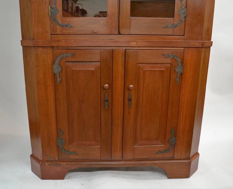 This is a massive and beautifully proportioned American half-glazed corner cupboard, built in two pieces in cherry wood. It is plain and simple in style, with a boldly swept crown and two glazed wide-swinging doors to the upper section and two