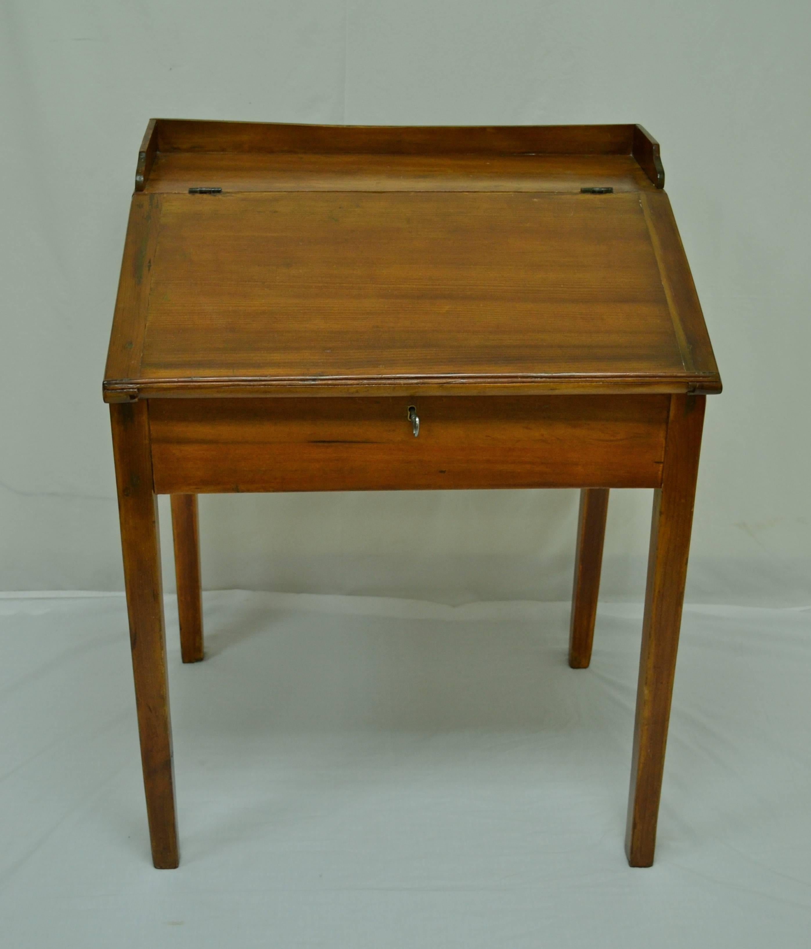 This is a handsome little pine and poplar schoolmaster’s desk on straight tapered legs. Beneath a slightly concave low gallery, the lift-top lid is mounted on original iron hinges. The working lock is period but not original and the key is a new