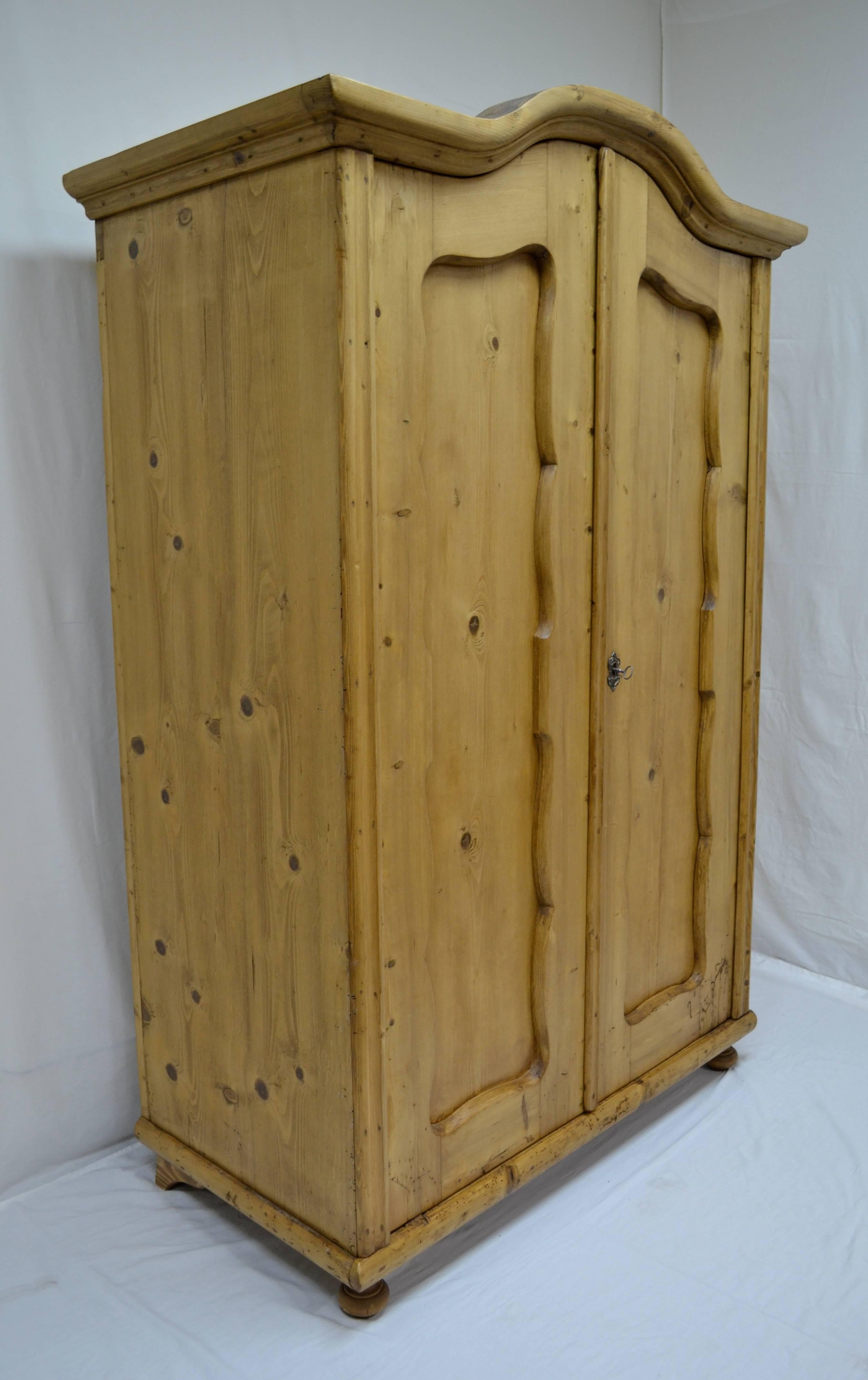 This is an unusually deep Baroque style pine armoire with a thick bonnet top crown molding. The door frames are scalloped to give beautiful curves to the panels, and arched to follow the line of the crown. The front corner moldings are a single bold