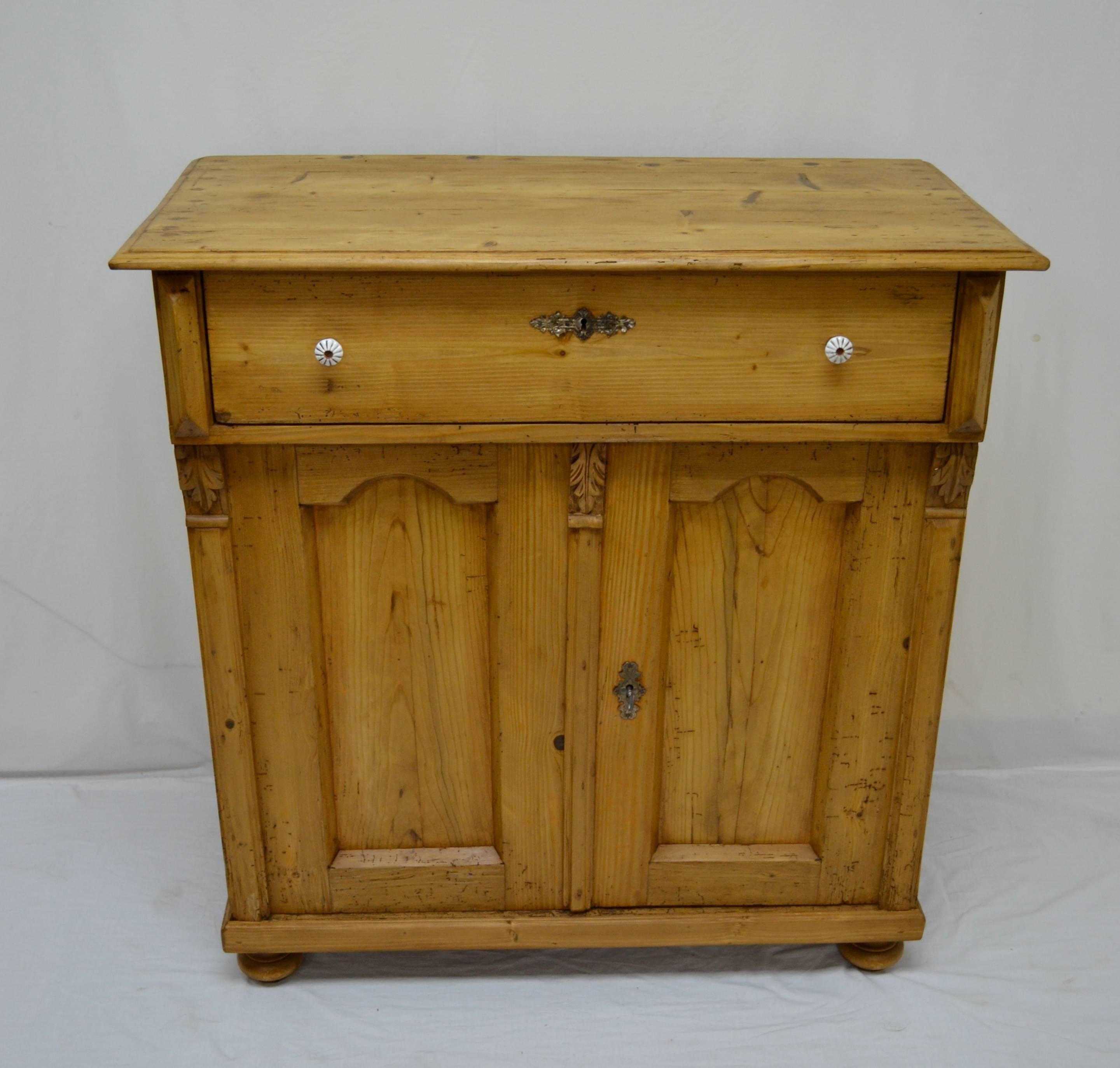 This is a very attractive tall and narrow pine dresser base. A single hand-cut dovetailed drawer sits above two doors with arched panels, flanked and separated by bold fluted molding and hand-carved acanthus leaf corbels. There is a single central